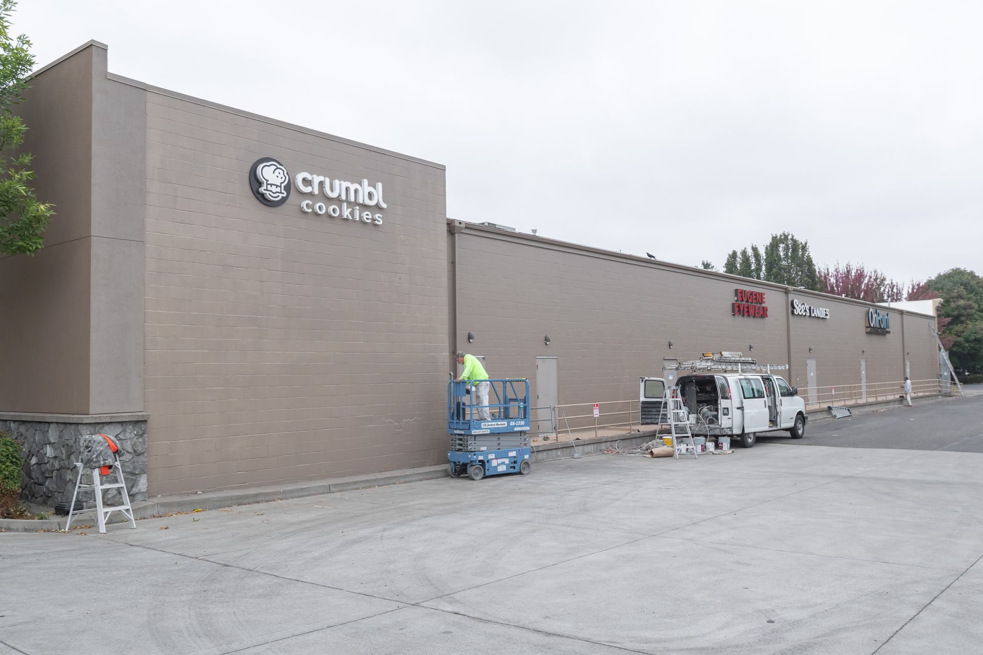 Exterior of a Crumbl Cookies storefront with a parking lot and pallets near the entrance