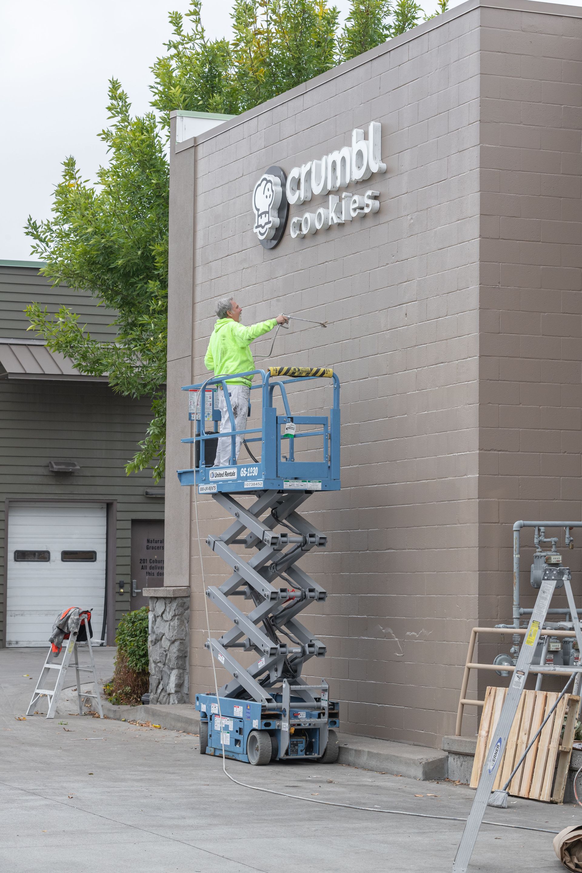 Worker on a blue lift installing a sign on a brown building exterior.