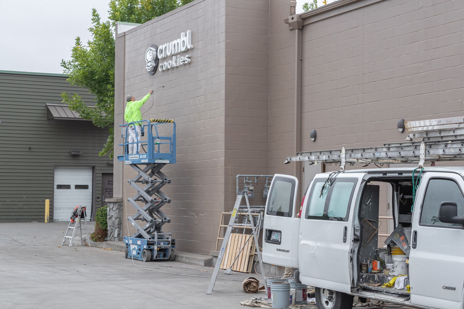 Workers on scissor lift near brick building exterior beside white service vans