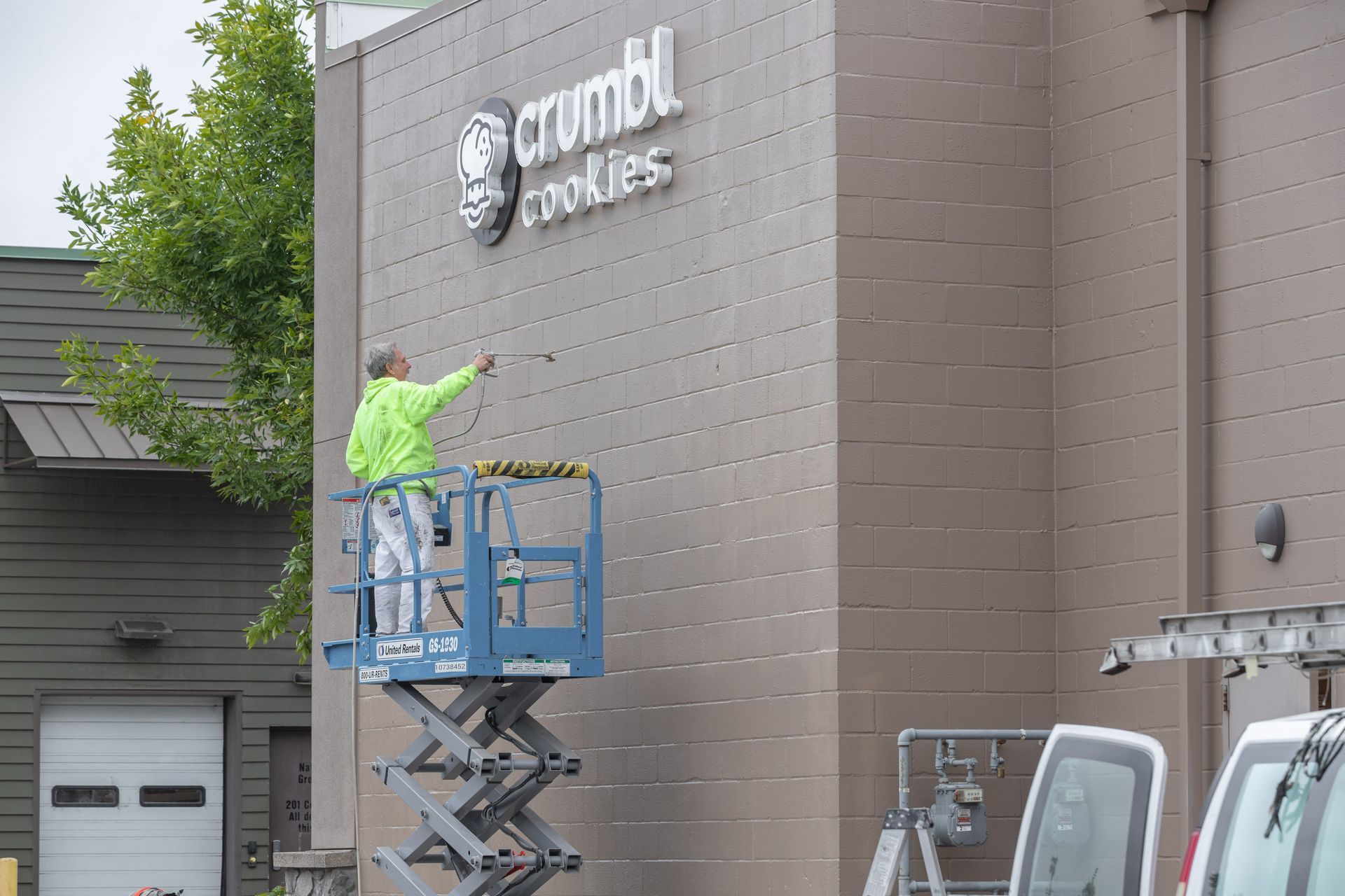 Worker on a blue lift installing a sign on a brown building exterior.