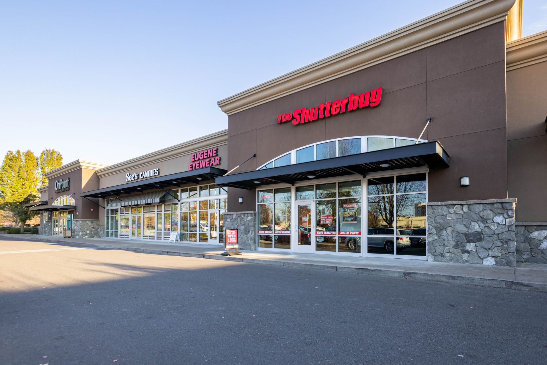 Strip mall storefronts with glass doors, stone accents, and red signage along an empty parking lot