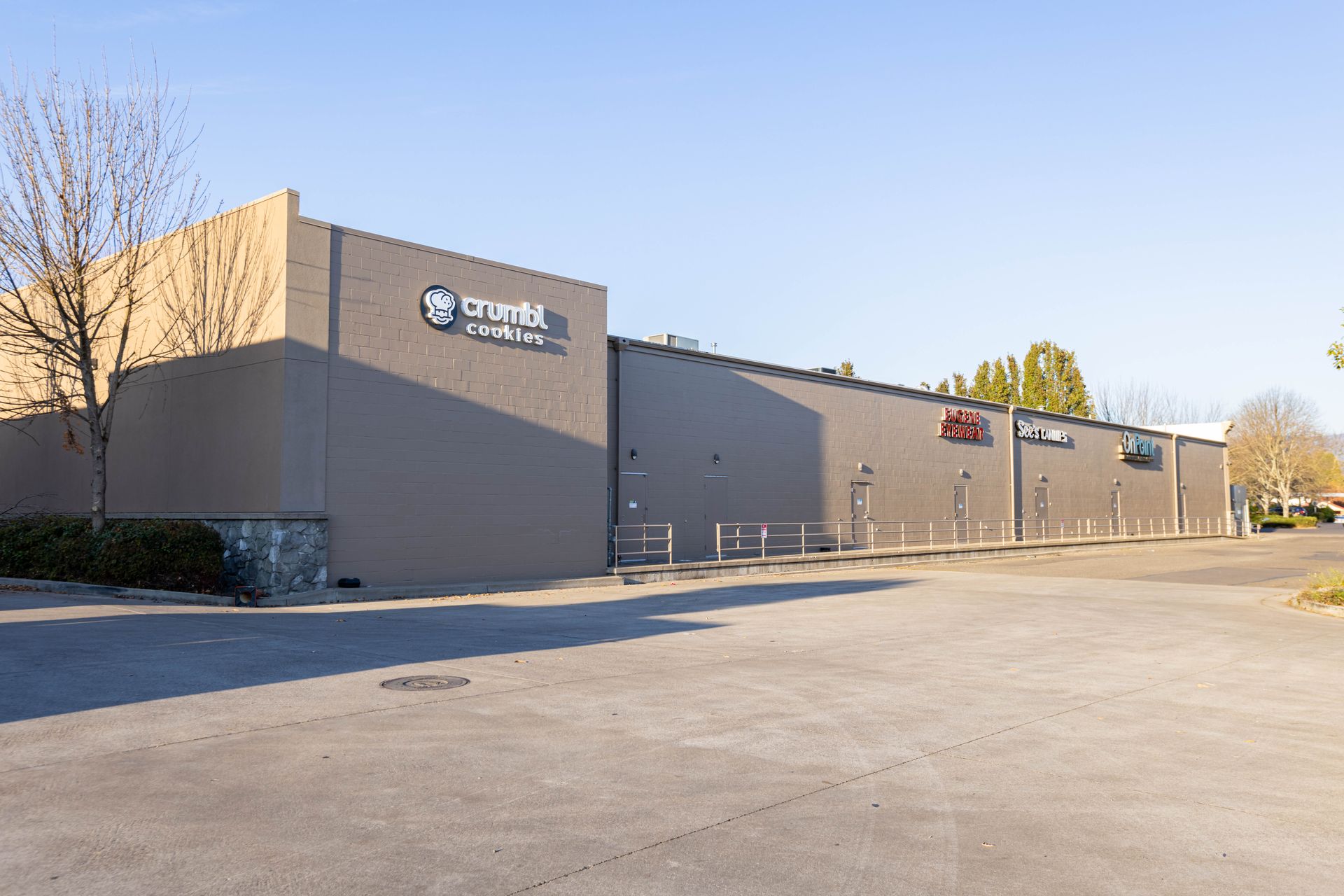Low tan commercial building with signage beside an empty parking lot under a clear sky
