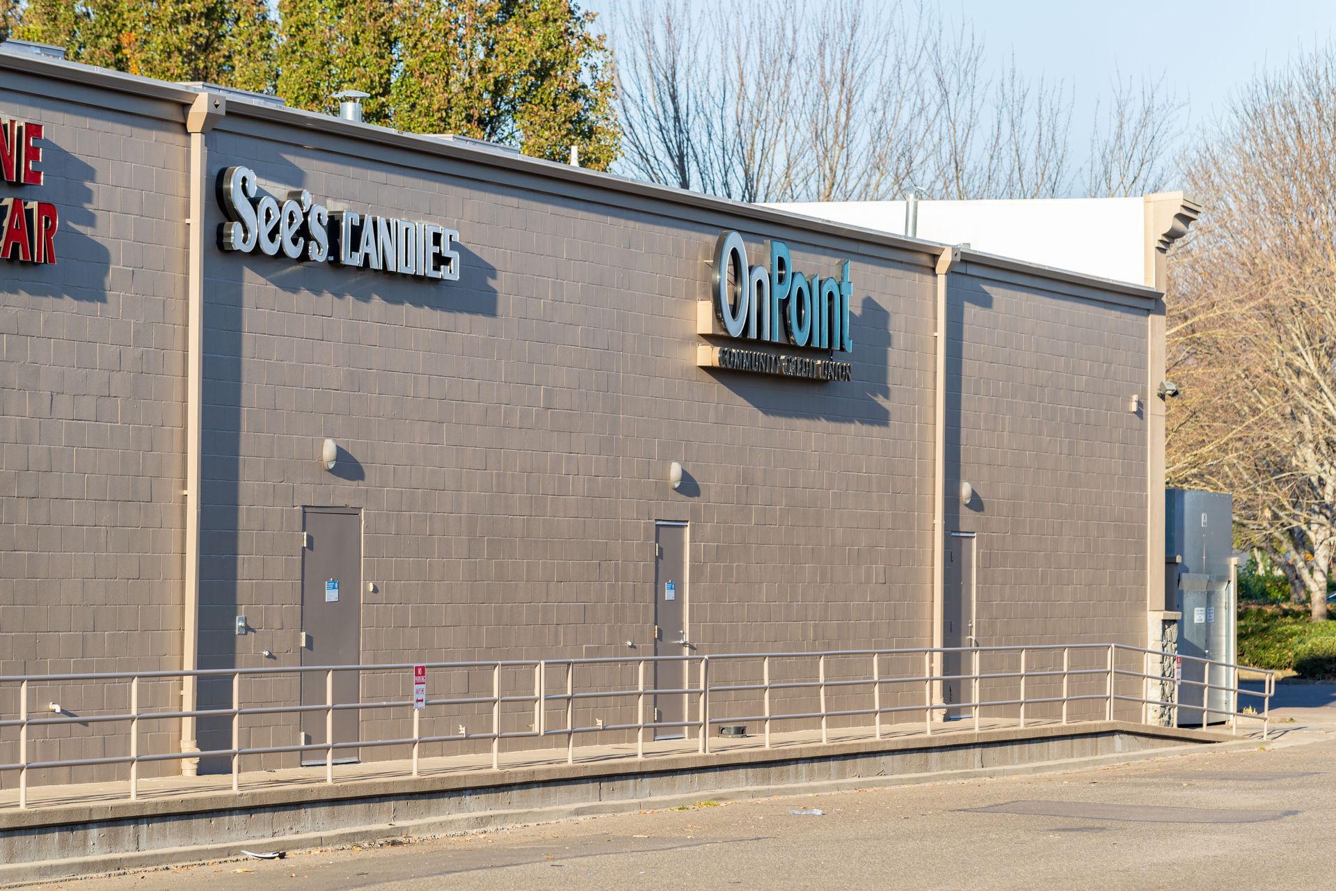 Exterior of a gray brick building with storefront signs and a metal railing in front