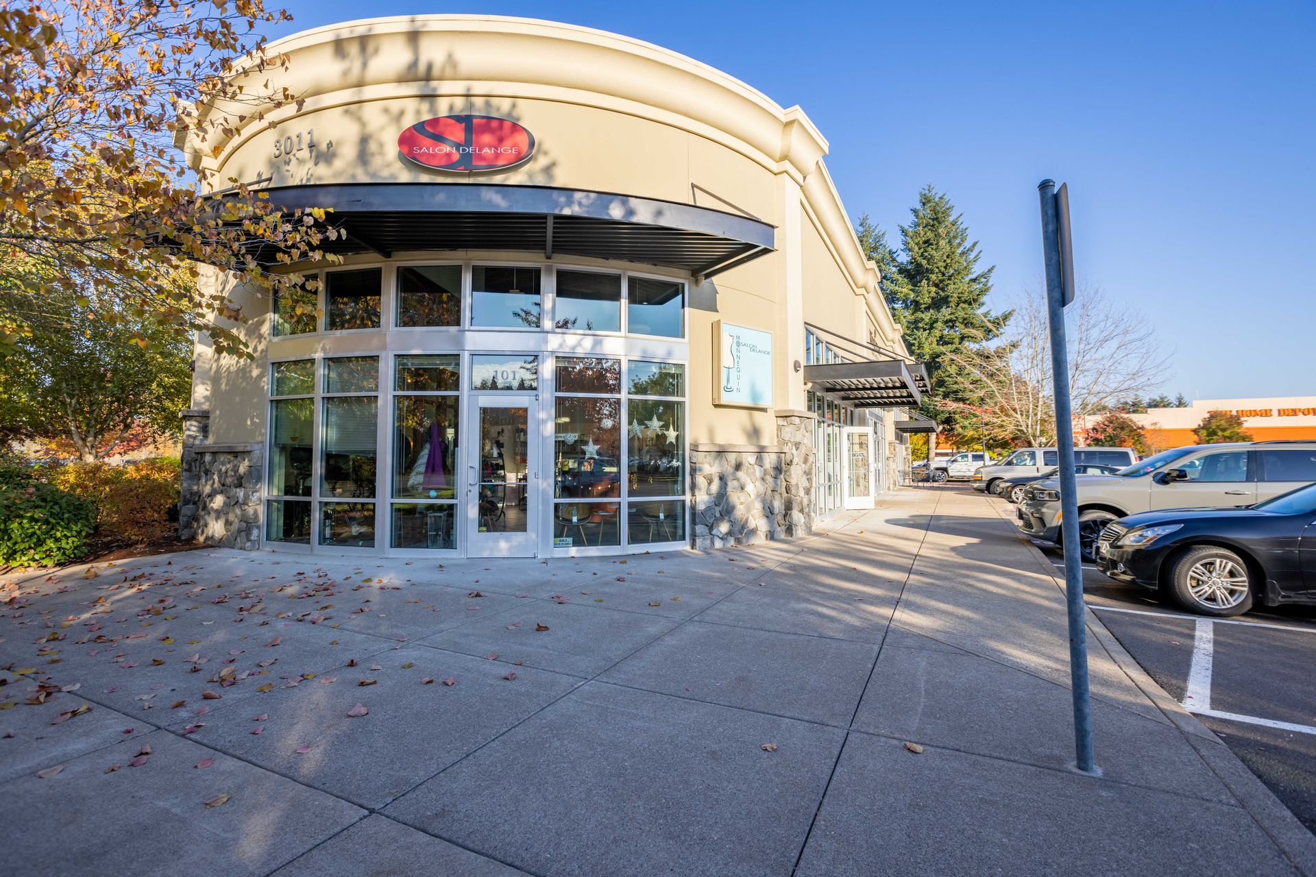 Storefront with glass entrance and red flower sign on a sunny street, with parked cars nearby