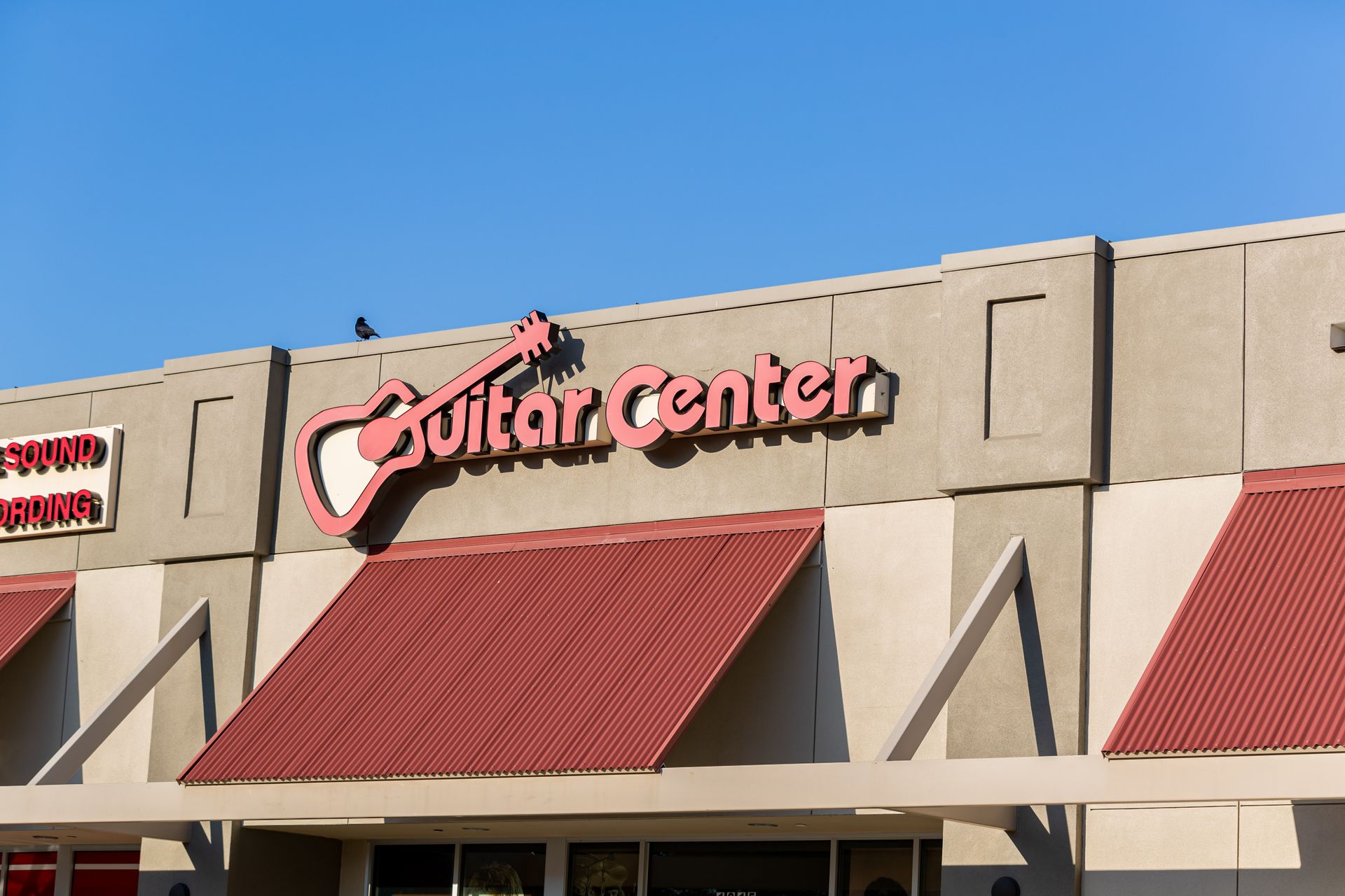 Guitar Center storefront with red awnings and beige exterior under a blue sky