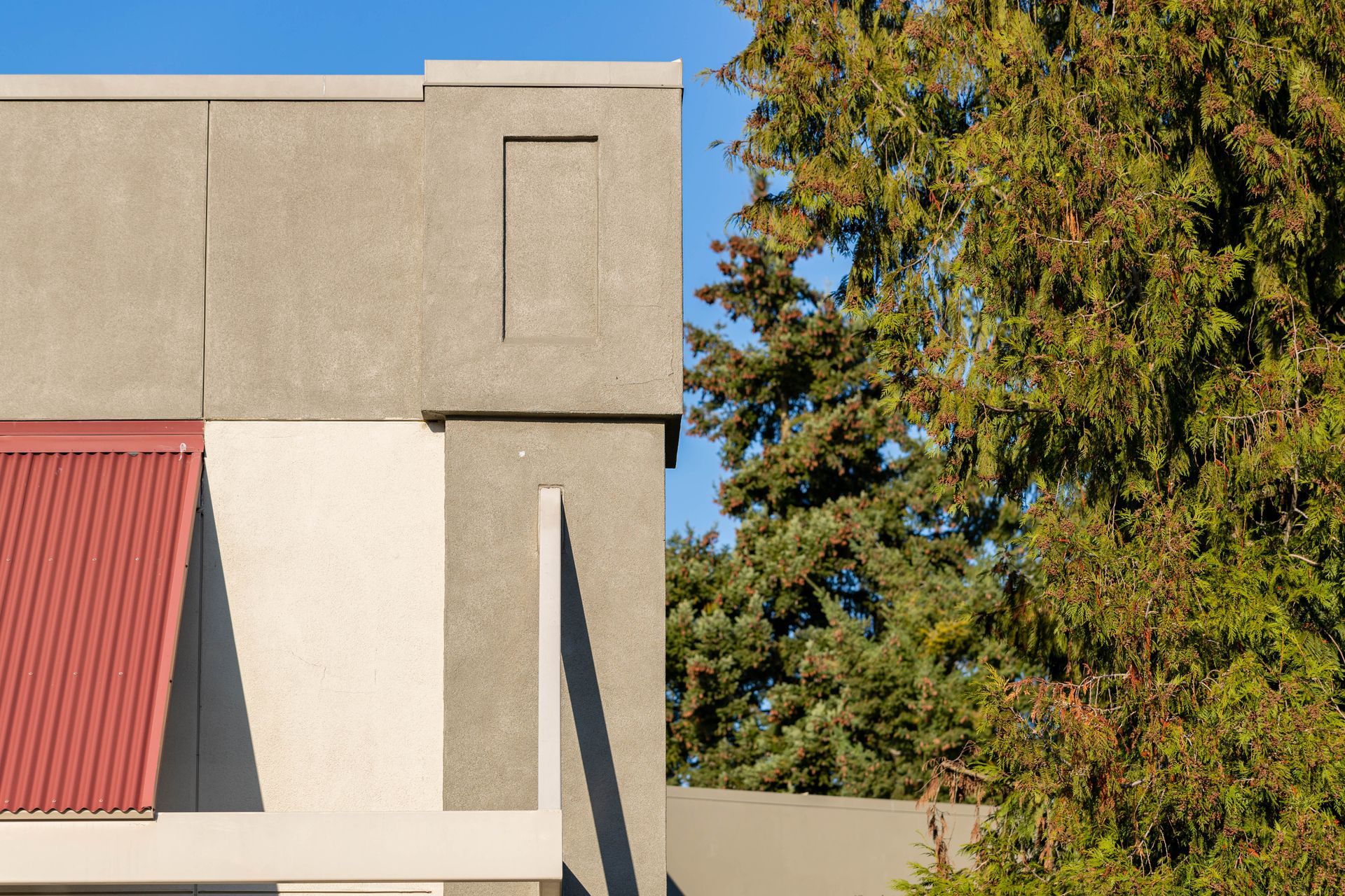 Modern building facade with red awning and trees against a blue sky