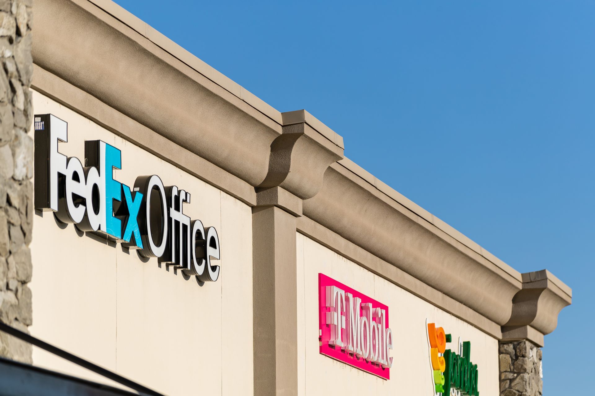 Storefront with a FedEx Office sign on a beige shopping center building under a blue sky.