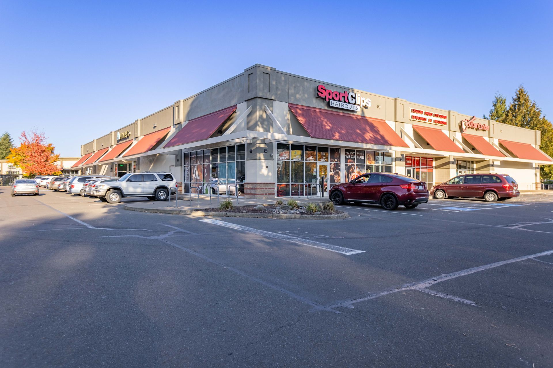 Shopping plaza with red awnings, parked cars, and a blue sky.