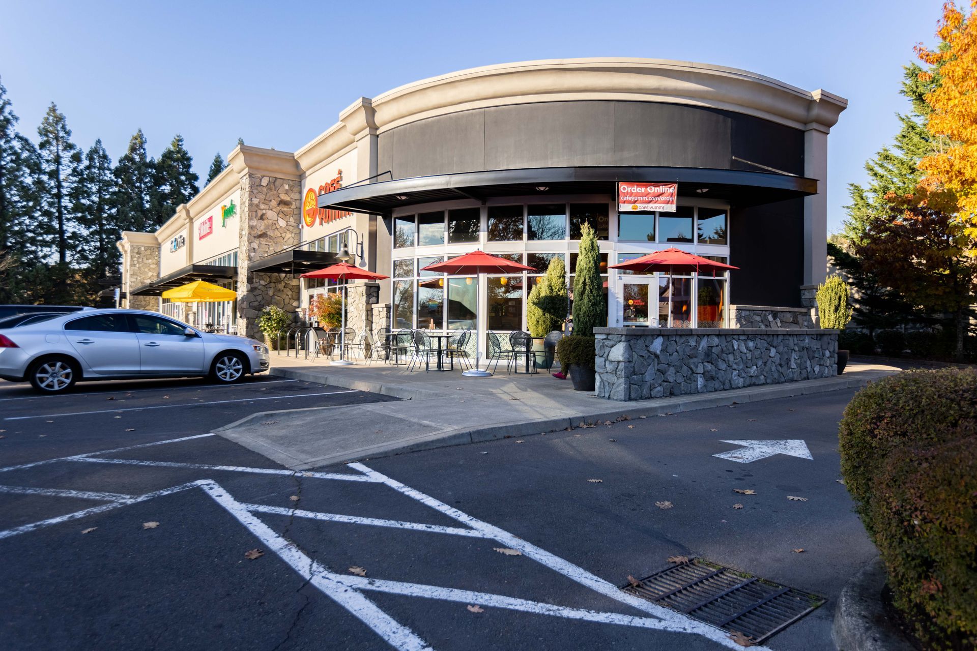 Modern restaurant exterior with glass windows, red awnings, and a parking lot in front