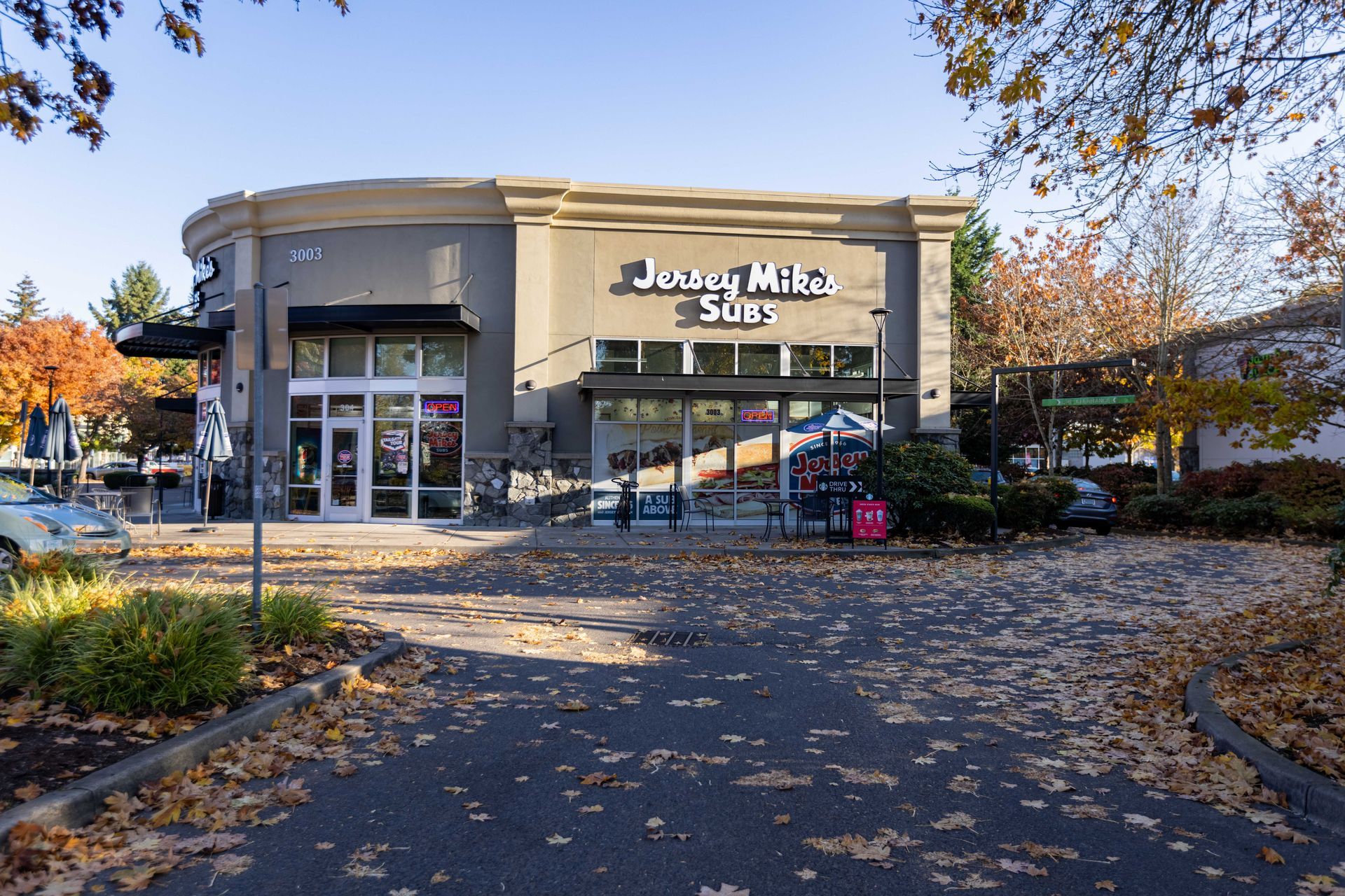 Jersey Mike’s Subs storefront with glass entrance, autumn trees, and leaf-covered walkway