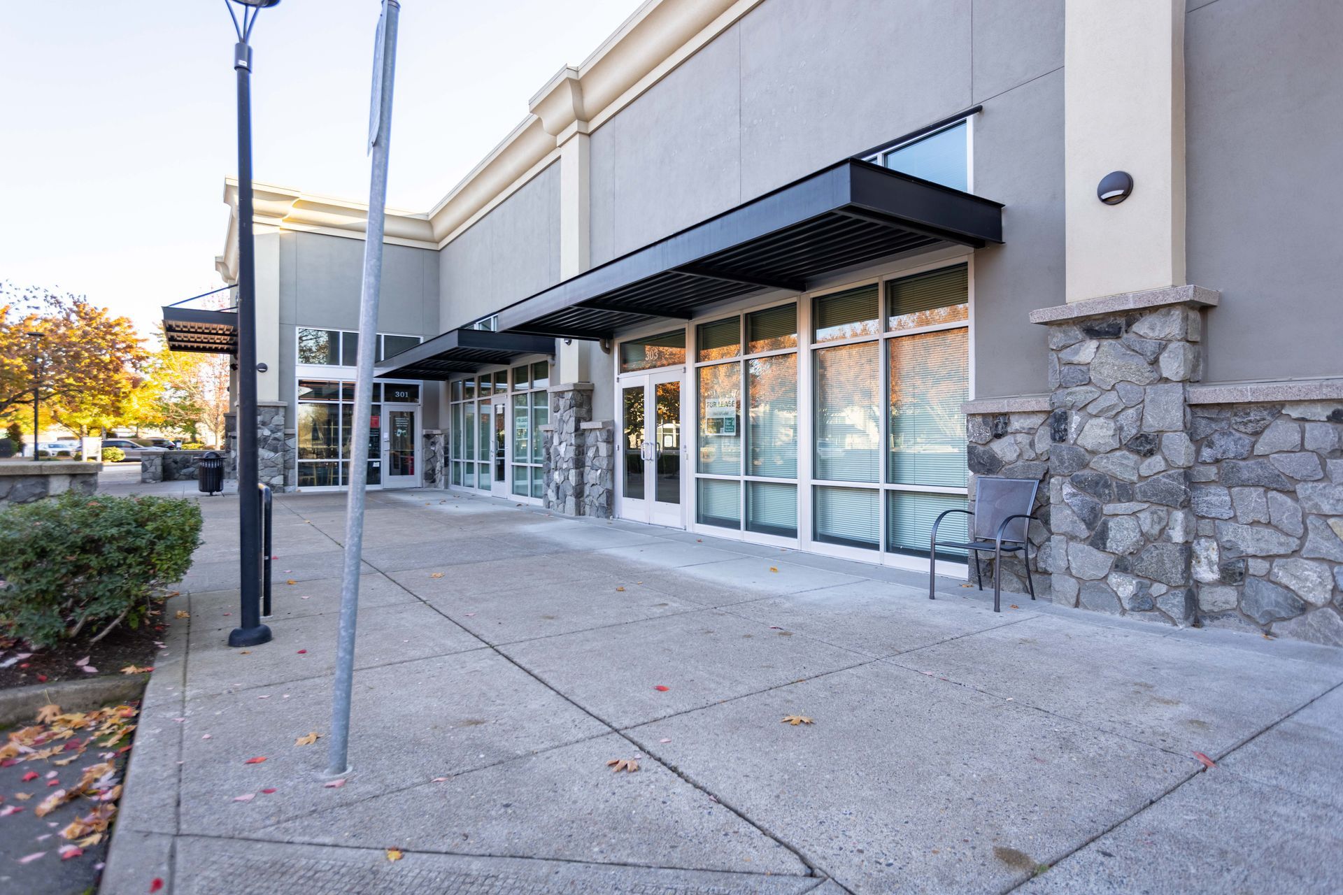 Storefront with glass doors, awnings, and stone facade along a concrete sidewalk