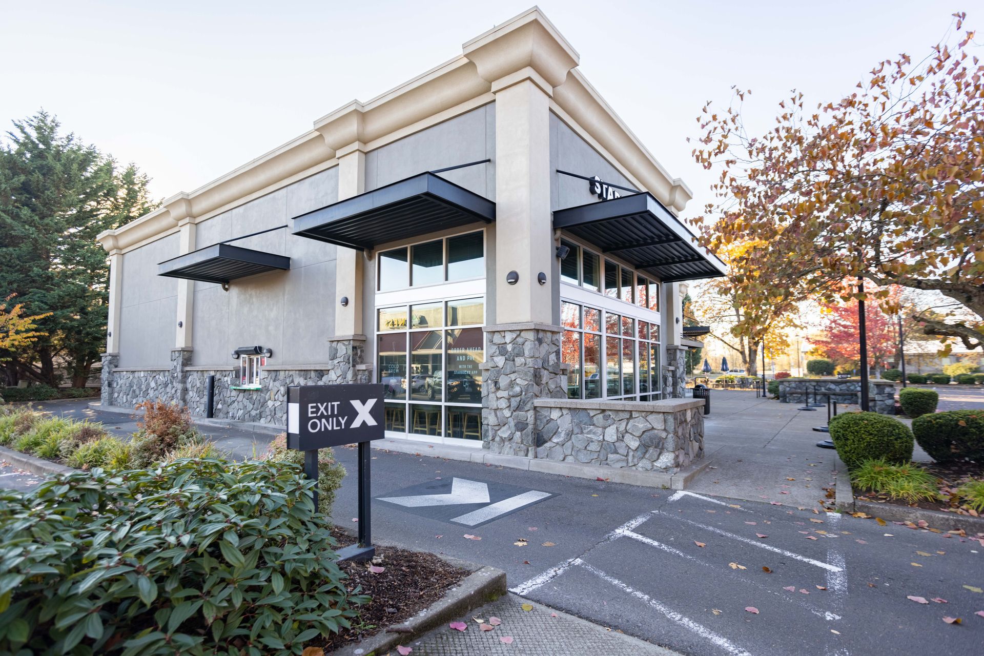 Modern storefront with large windows and black awnings beside a landscaped walkway at sunset