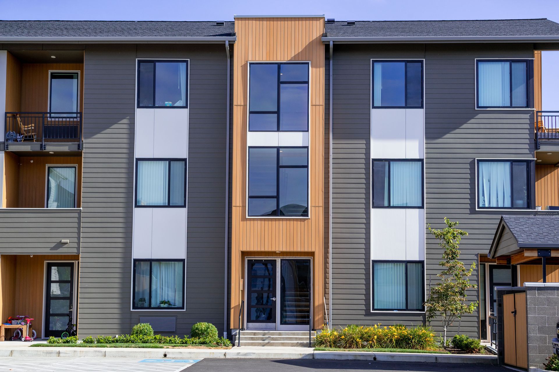 Modern apartment building facade with gray siding, wood accents, balconies, and large windows