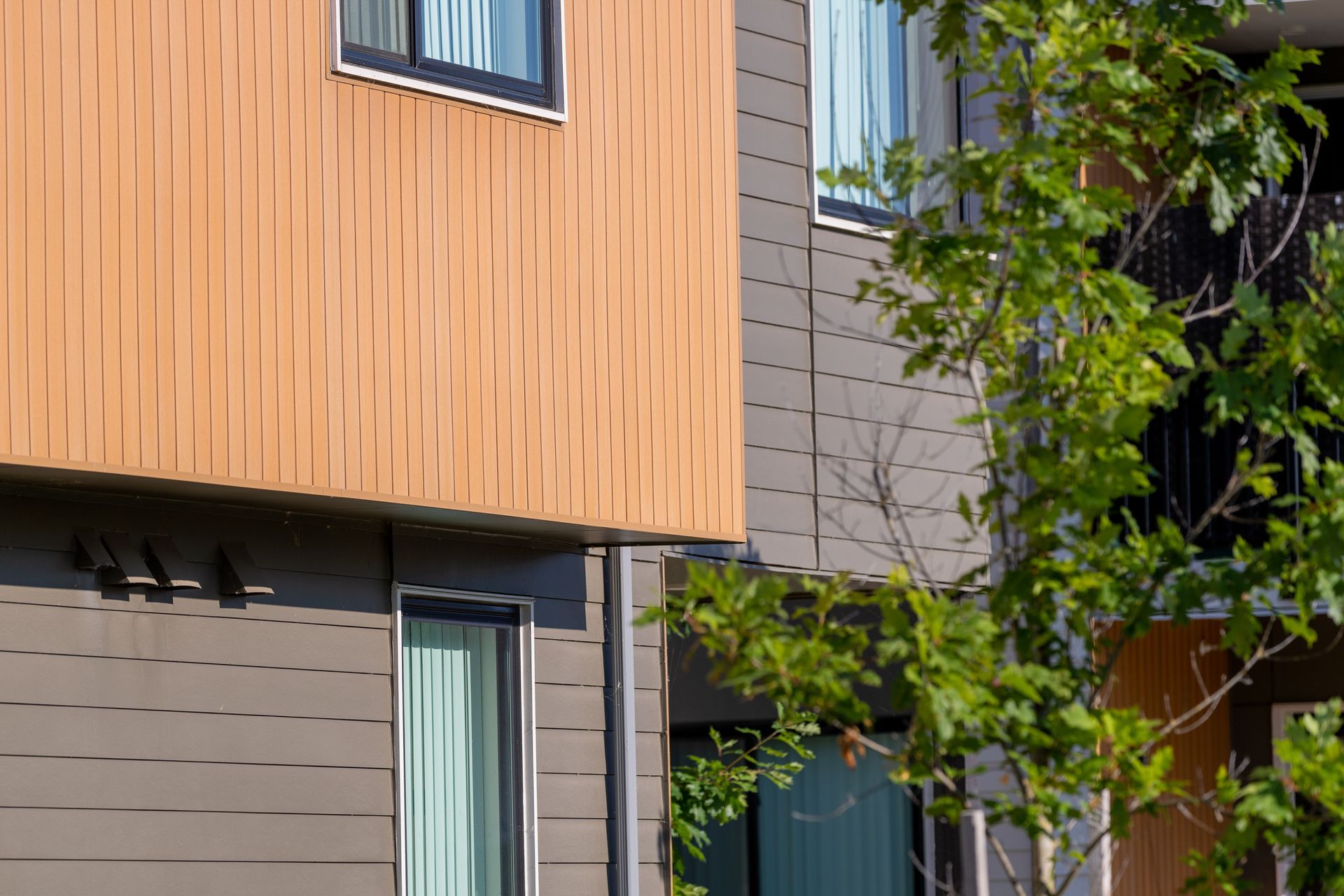 Modern apartment building facade with orange and gray panels and a leafy tree in front