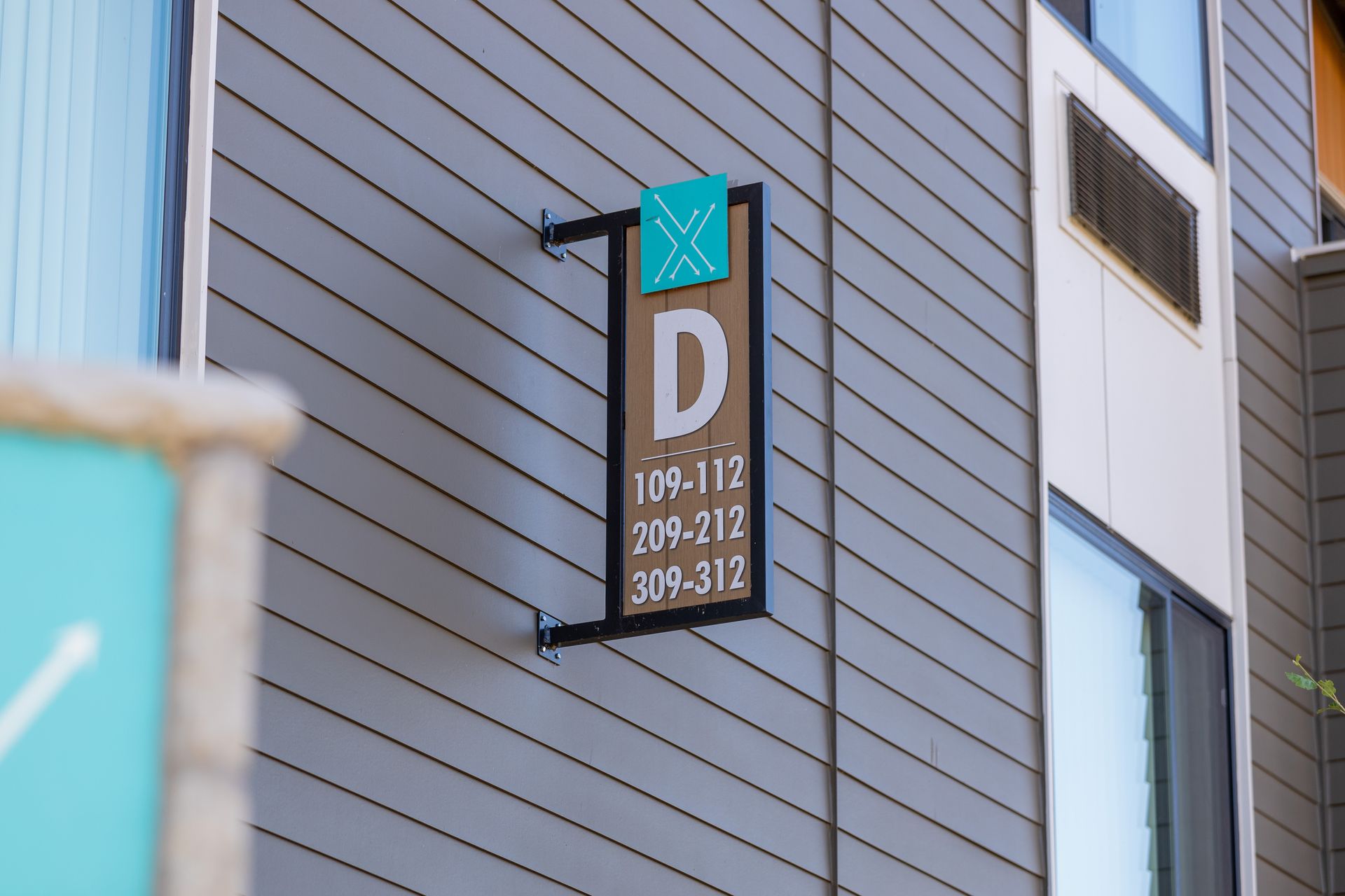 Building-mounted sign with a large white “D” and unit numbers on a gray exterior wall.