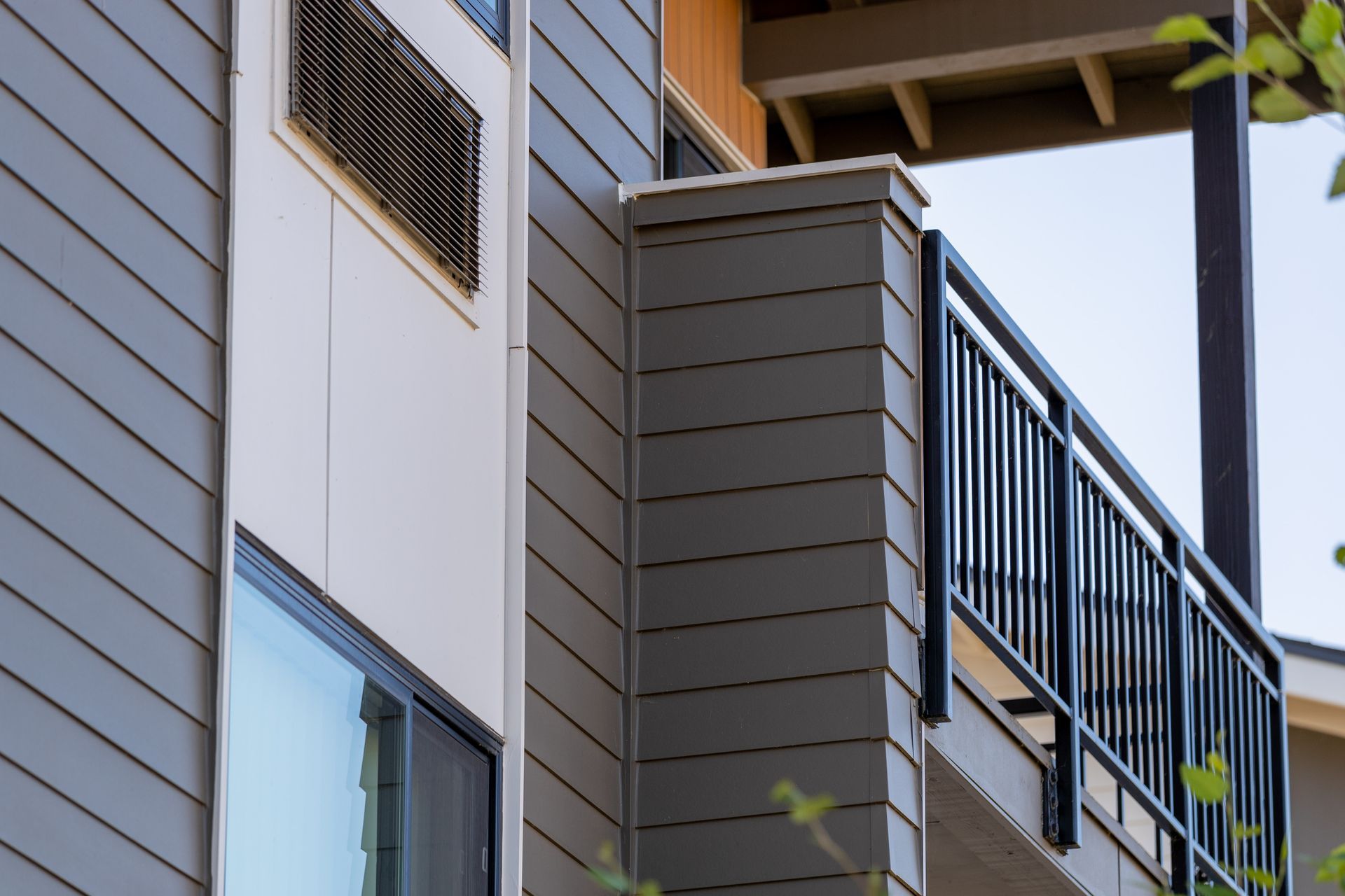 Apartment balconies with gray siding and black railings, viewed from below
