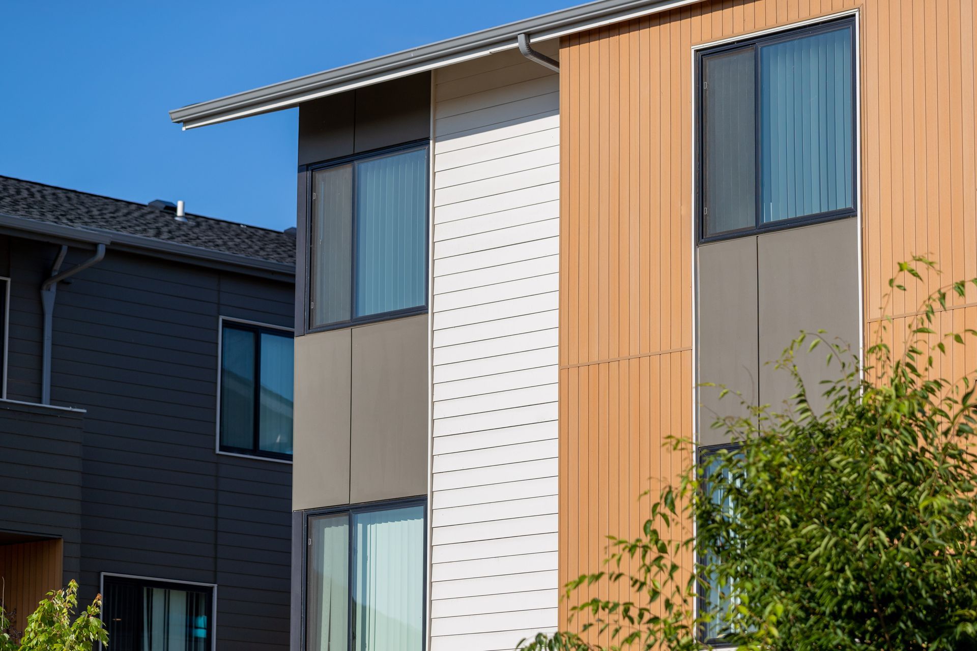 Modern apartment facade with wood, white, and gray panels and large windows under a blue sky