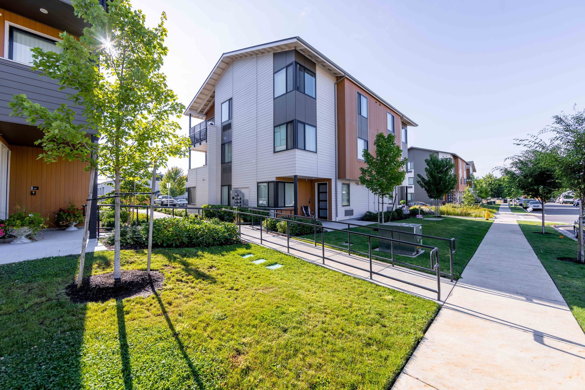Modern apartment buildings beside a sidewalk and landscaped lawn on a sunny day