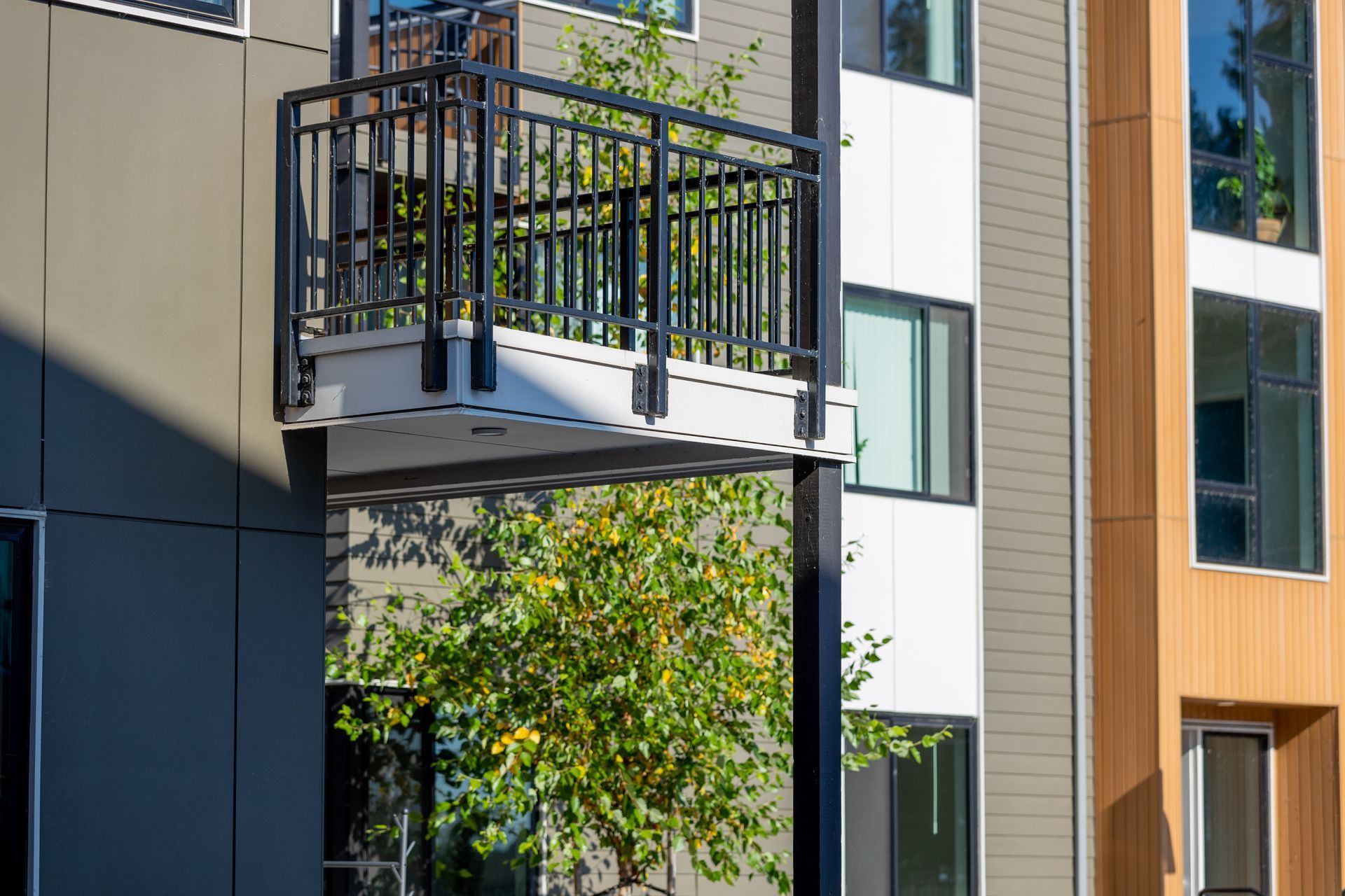 Modern apartment building balcony with black railing and a green tree below