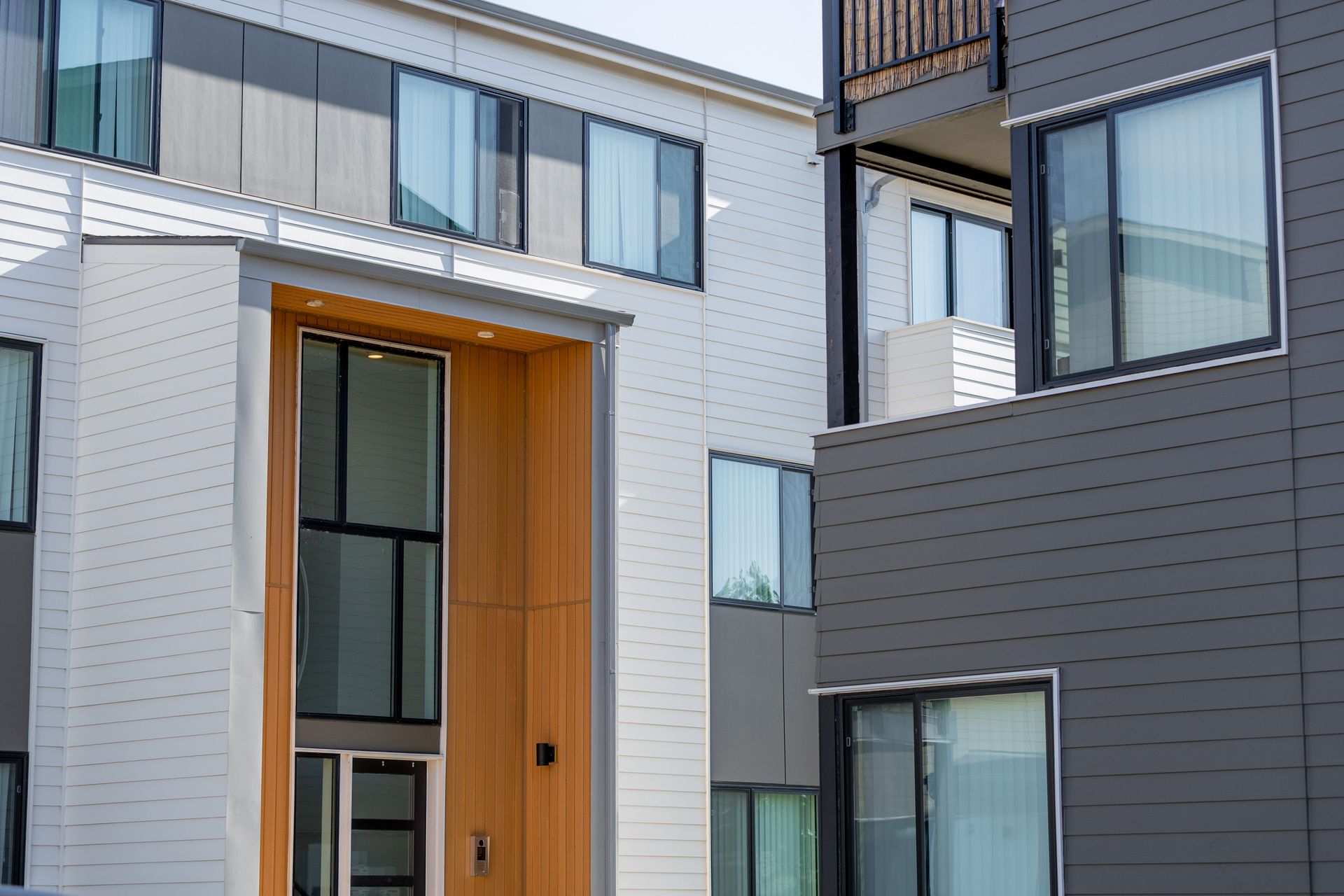 Modern apartment exterior with gray siding, white brick, and tall windows around a wood-framed entryway