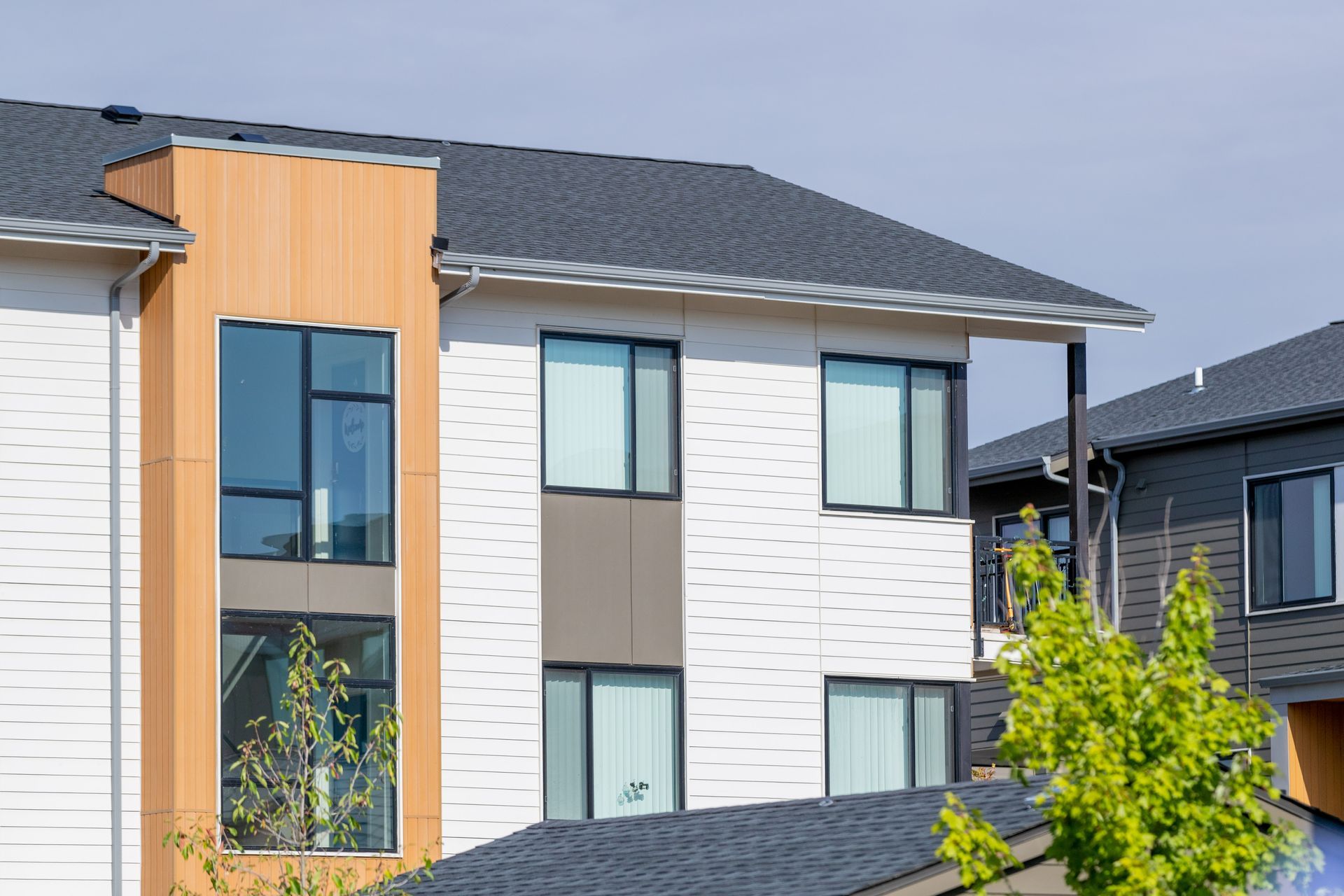 Modern two-story house exterior with white and beige siding, dark roof, and large windows
