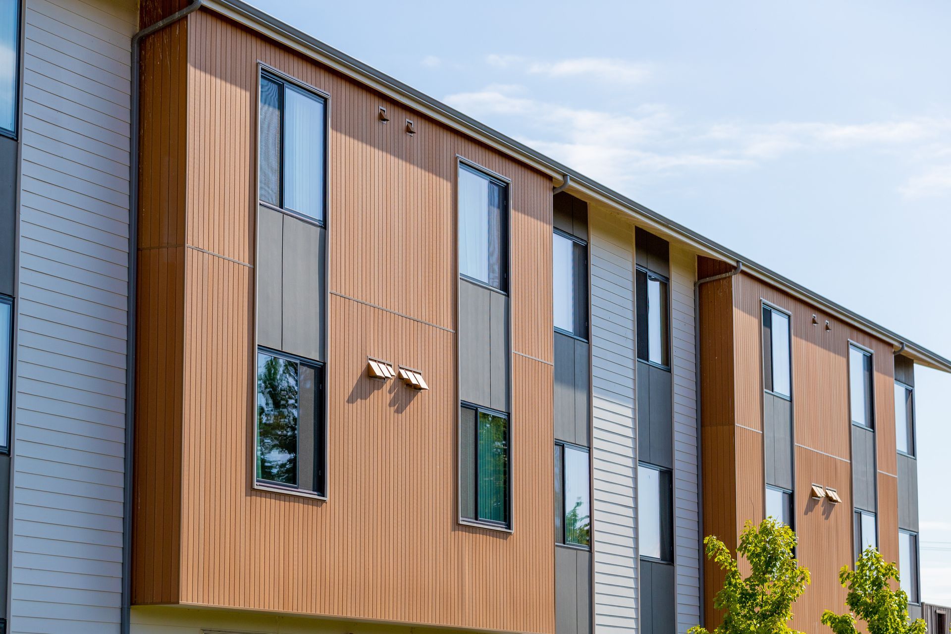 Modern apartment building exterior with wood siding, narrow windows, and gray panels under a blue sky