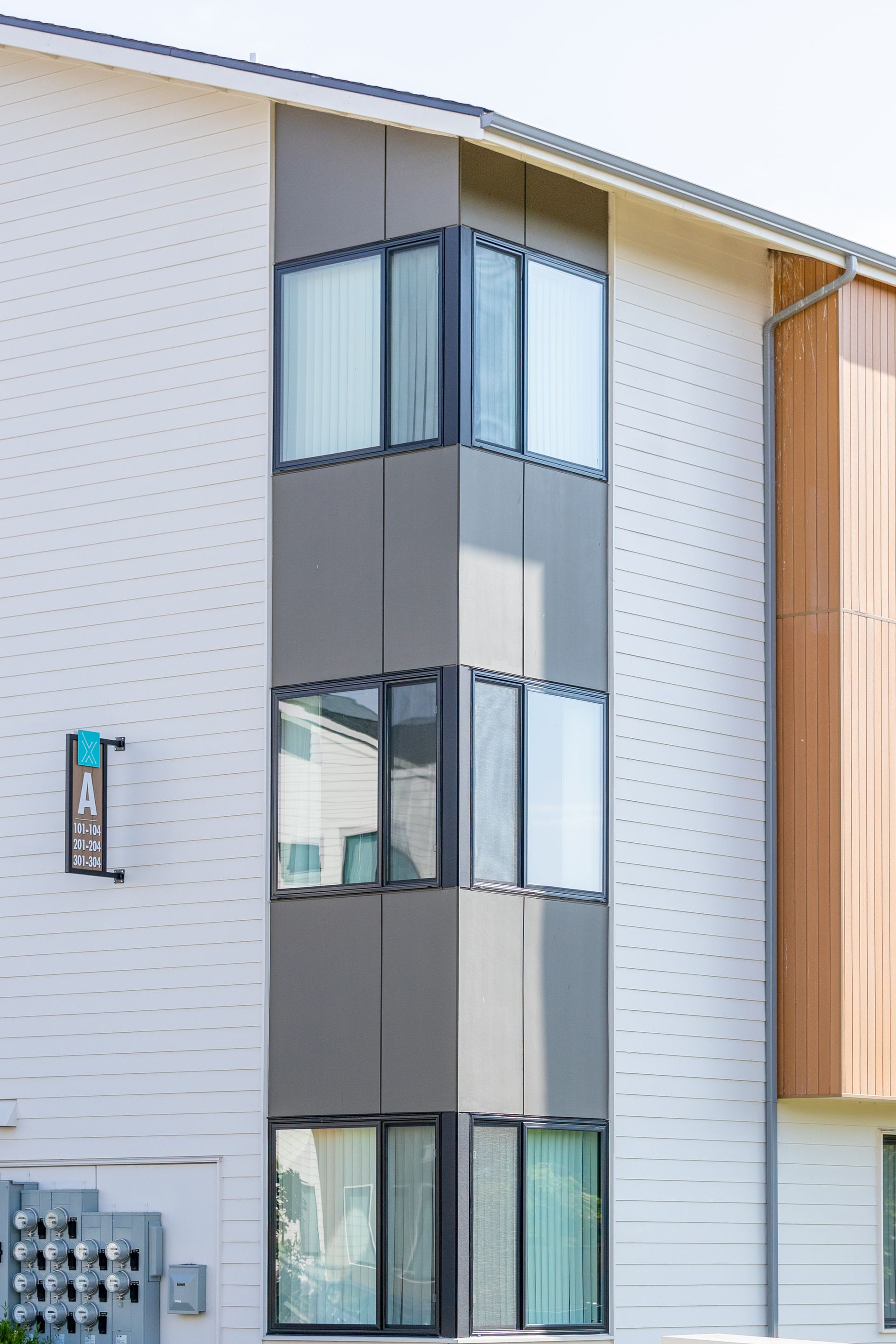 Narrow glass-and-gray stair/elevator tower on the exterior of a modern building.