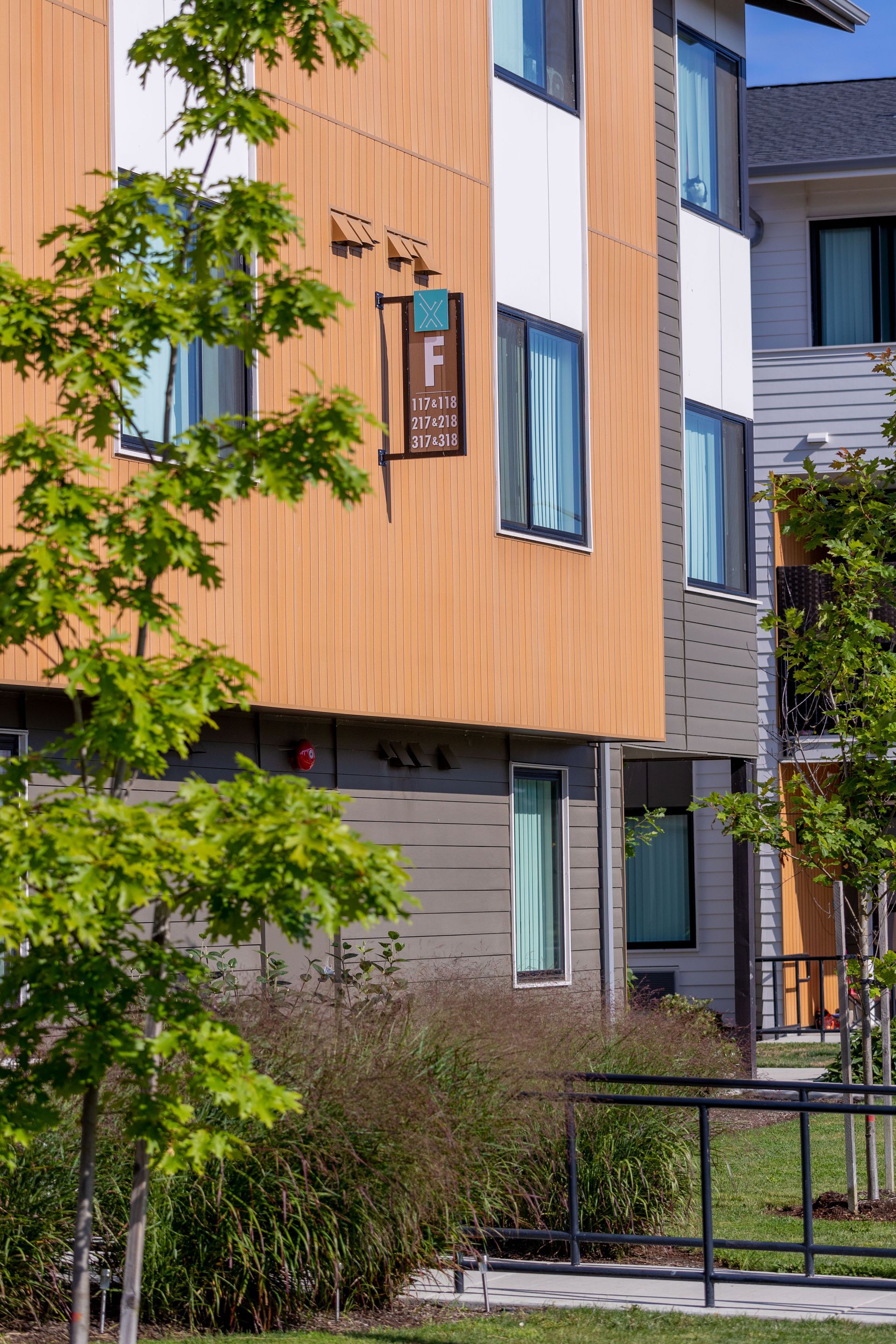 Modern apartment building with orange wood siding, gray brick, and trees in front