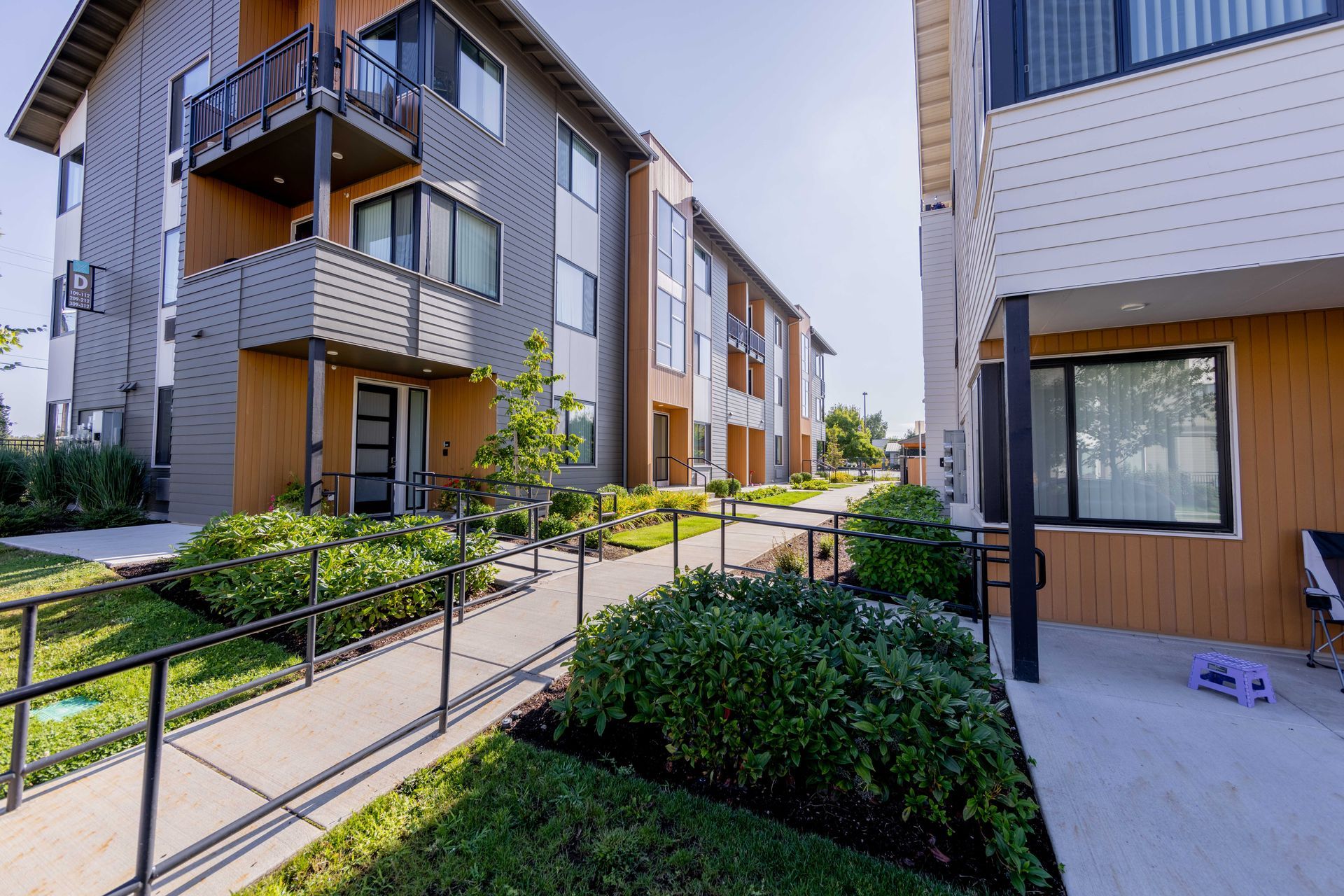 Modern apartment courtyard with walkways, greenery, and balconies on sunny day