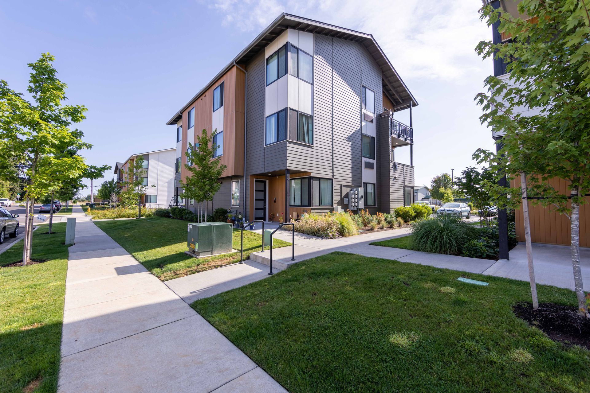 Modern apartment building beside a sidewalk and green lawn on a sunny day