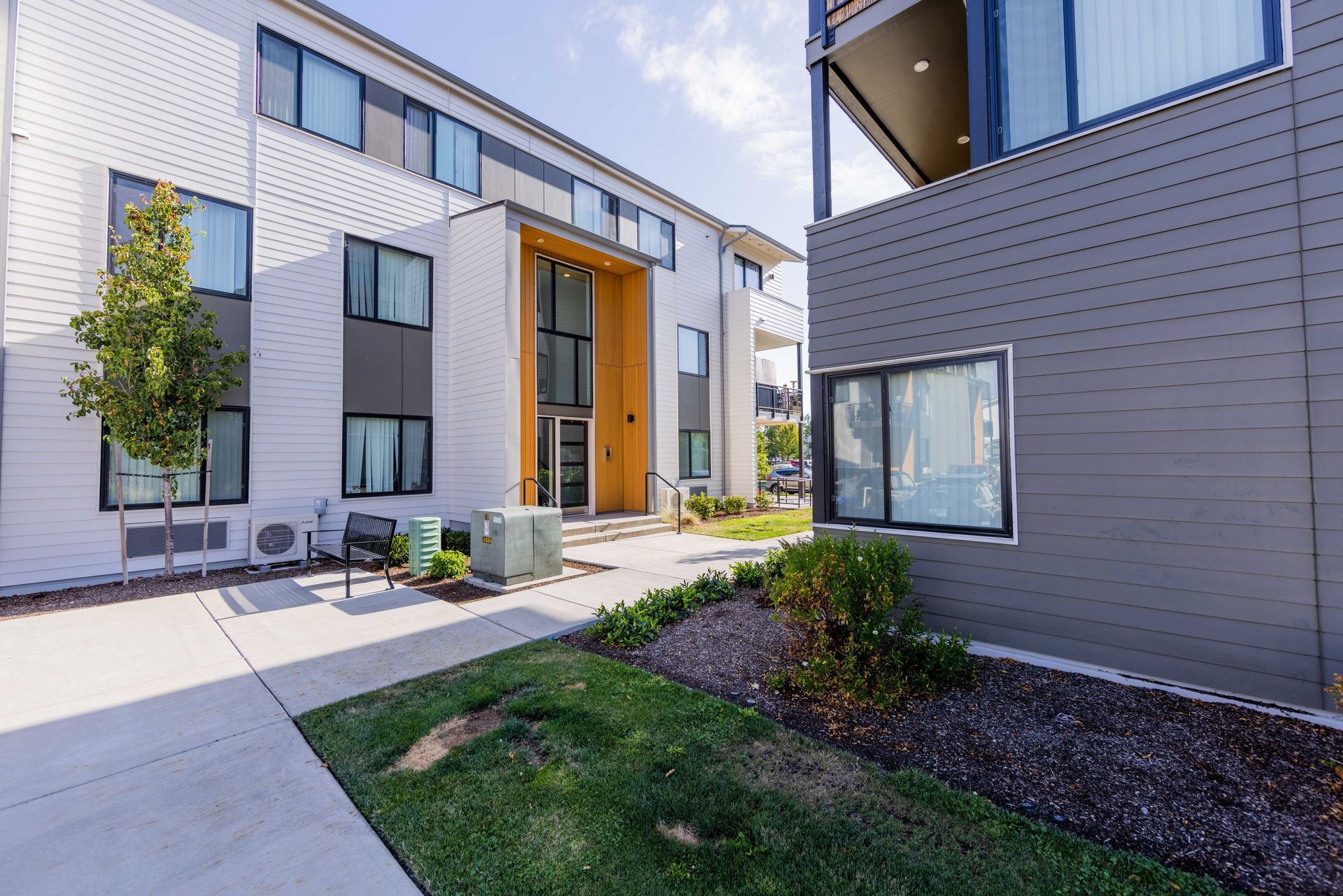 Modern apartment courtyard with white and gray buildings, windows, and a small grass and walkway area.