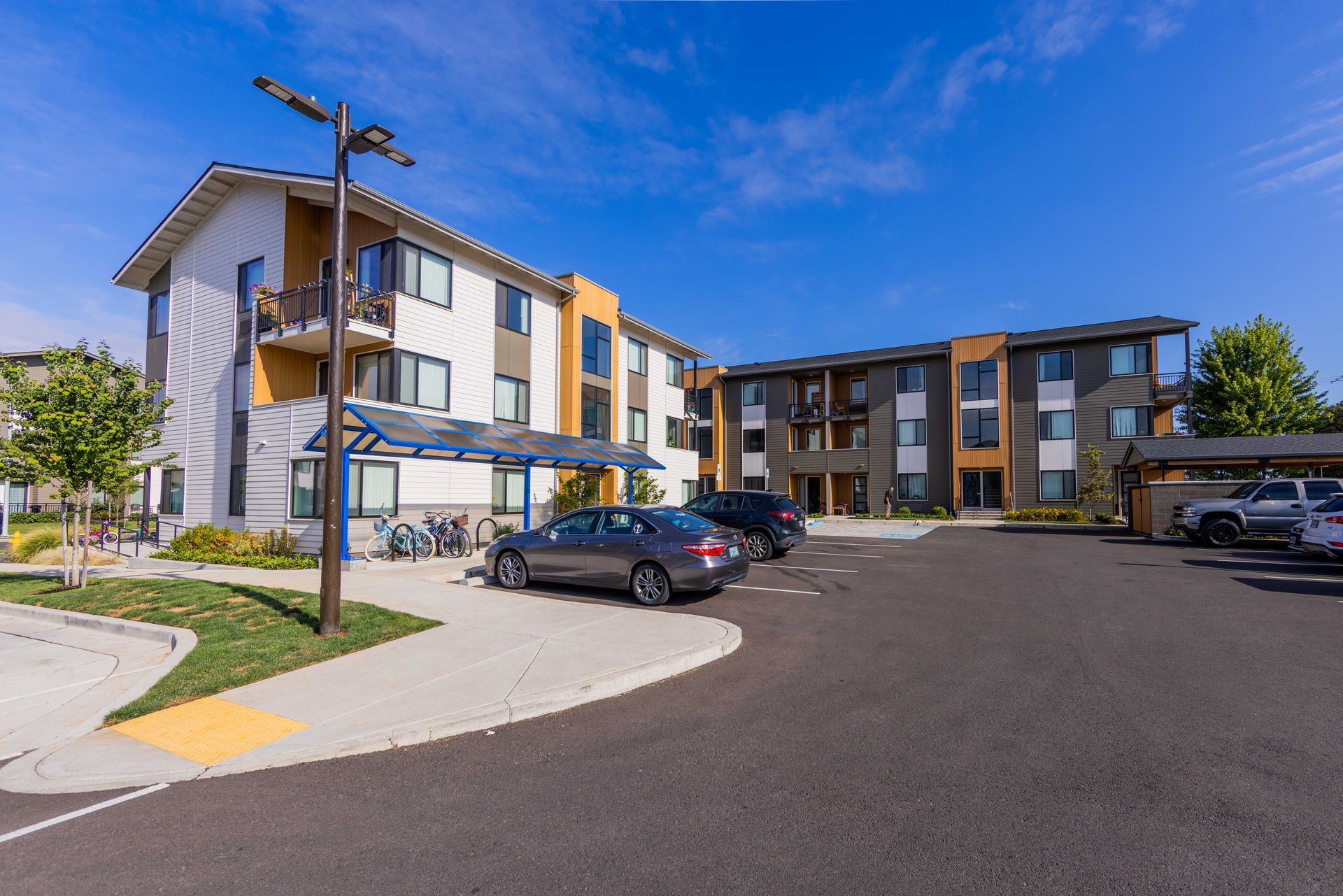 Apartment complex with parked cars and a blue awning under a clear sky