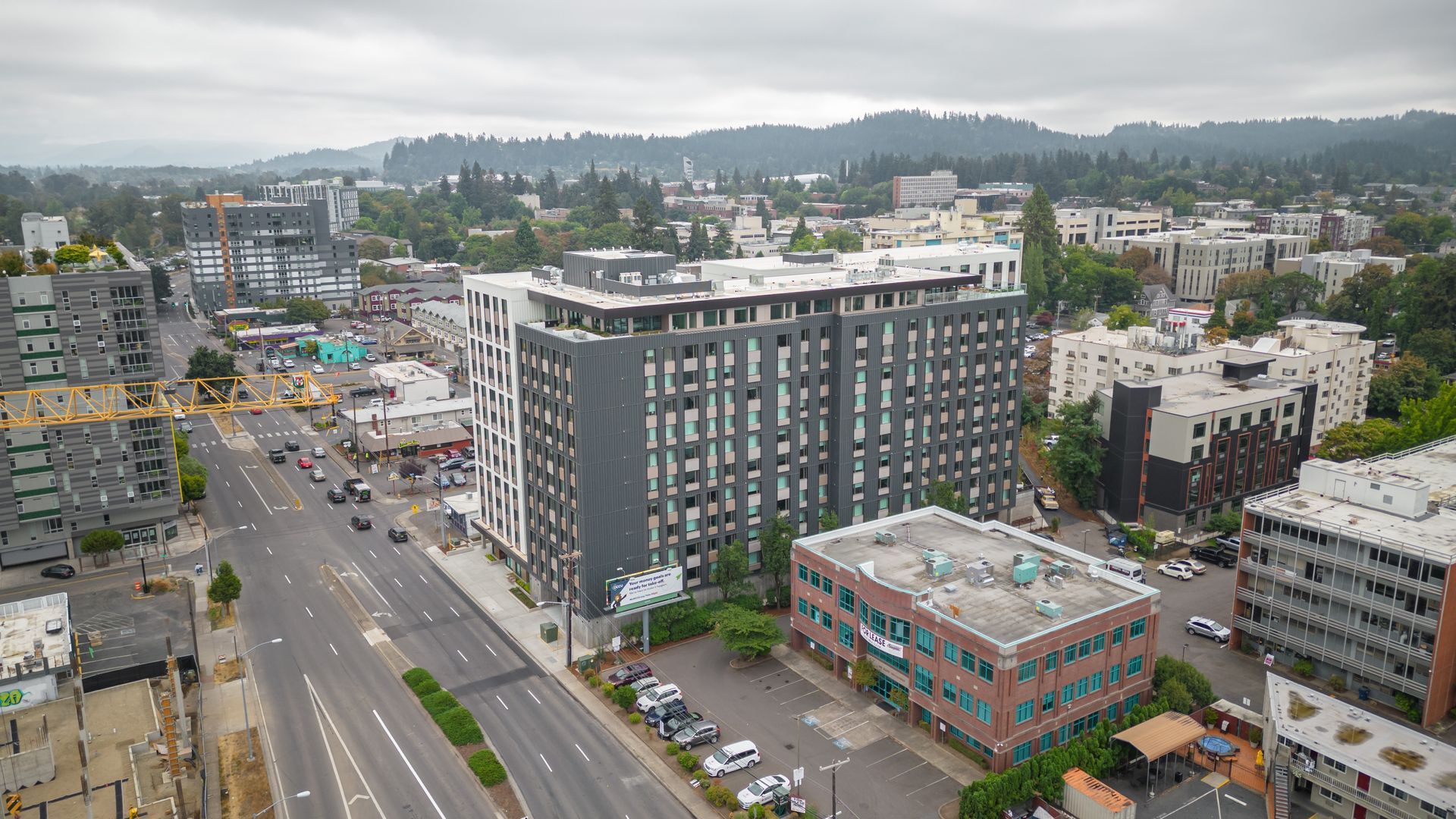 Aerial view of a city street with a tall apartment building, brick office block, and hills in the background
