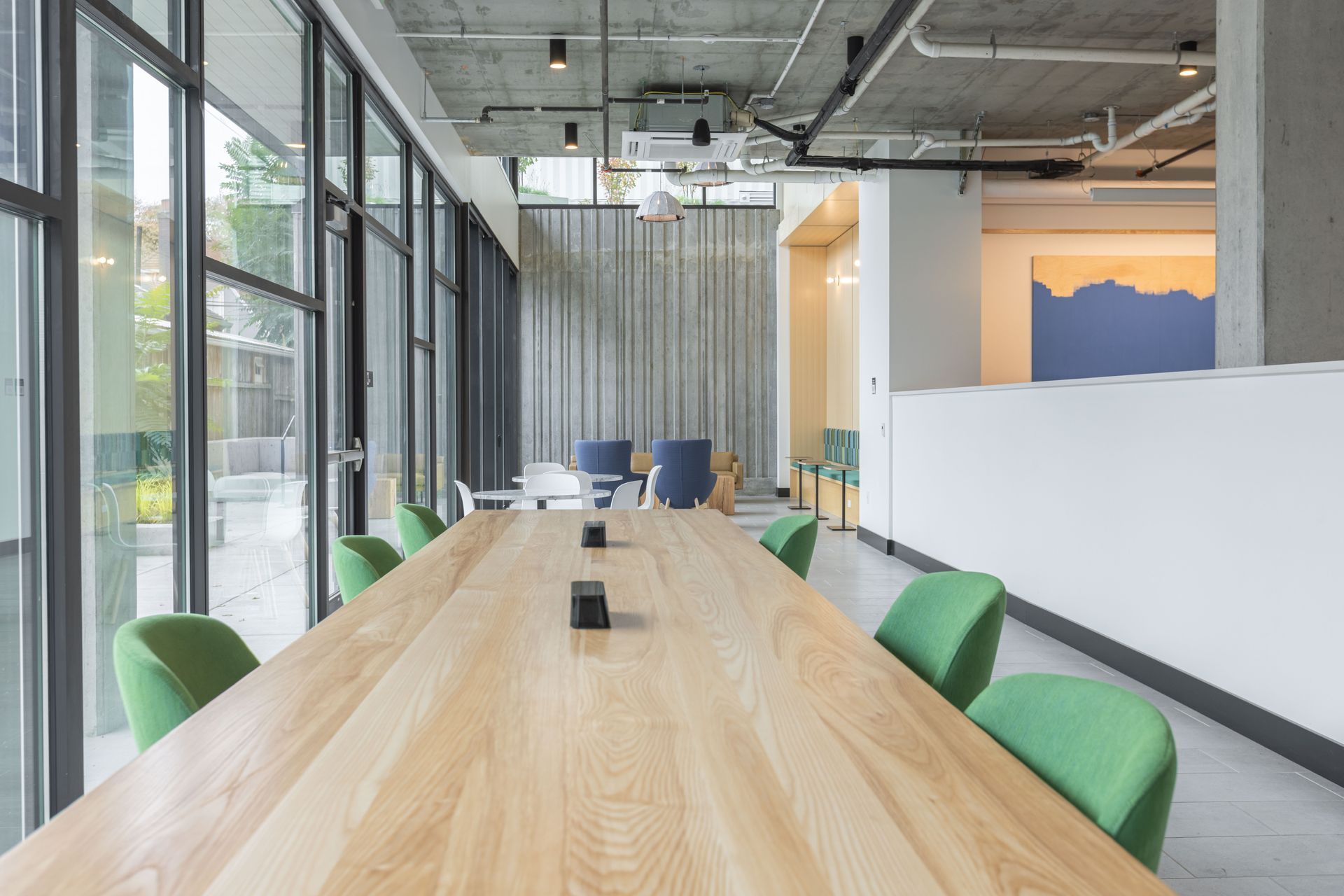 Modern conference room with a long wood table, green chairs, and floor-to-ceiling glass walls