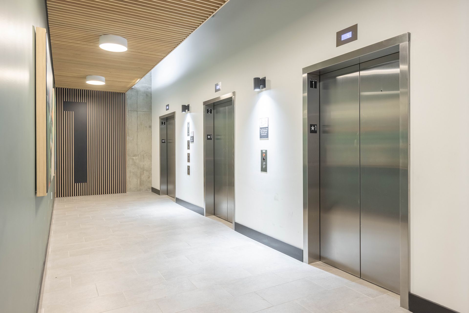 Modern hallway with two stainless steel elevators and a wavy wood ceiling under bright lighting