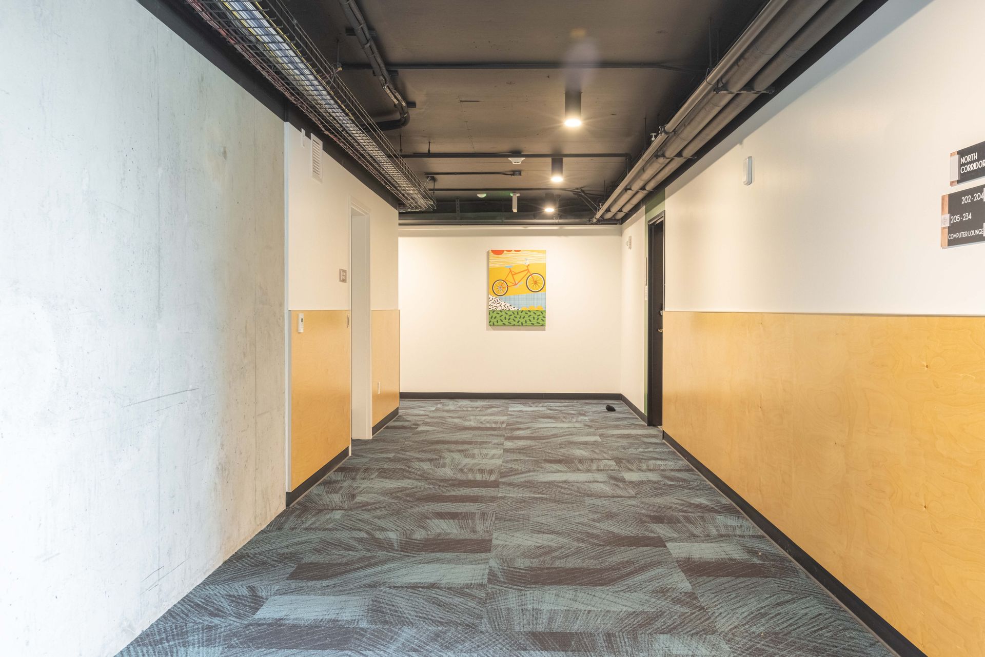 Empty hallway with white and tan walls, dark ceiling, and a framed picture at the far end.