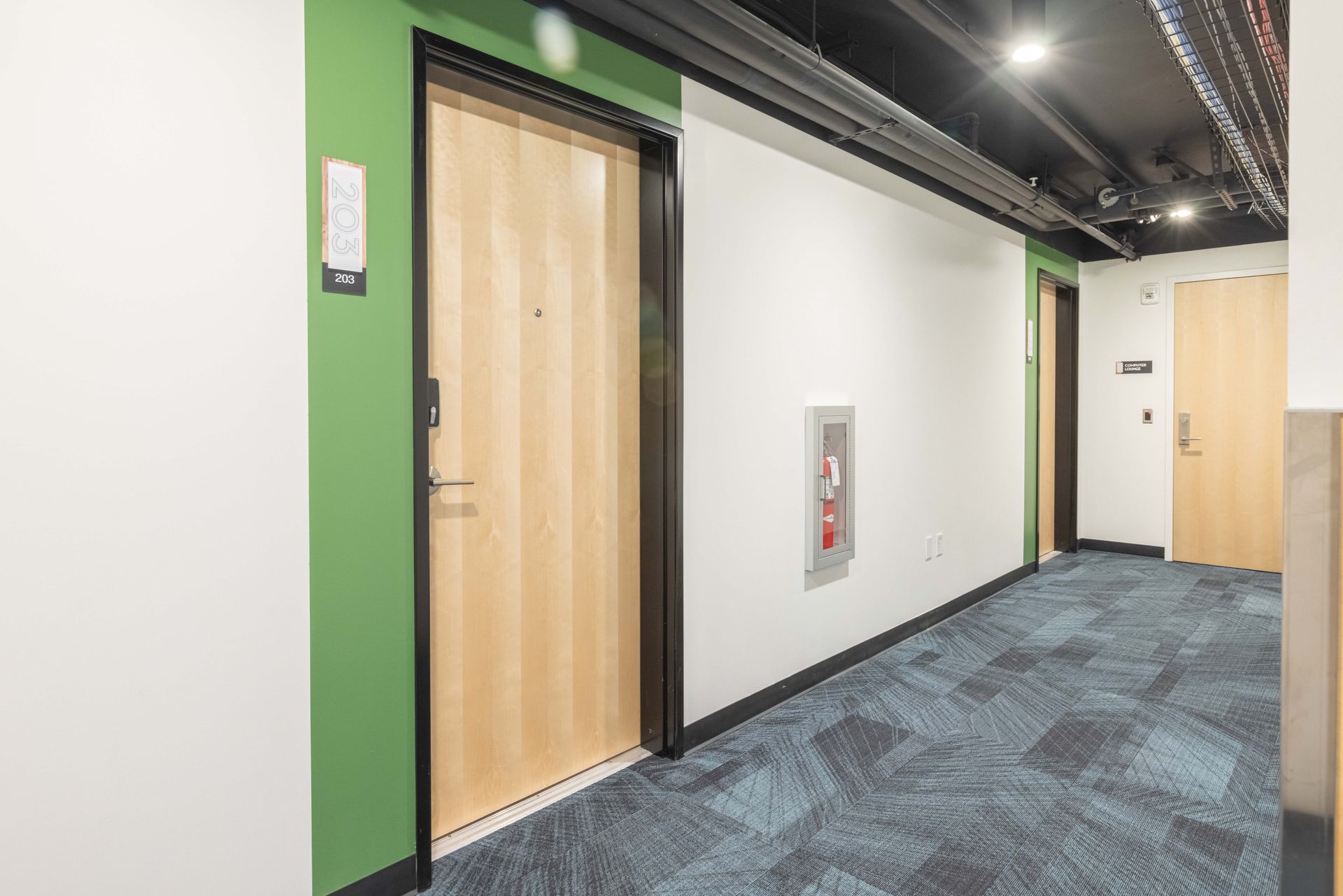 Office hallway with green and white walls, wood doors, and blue patterned carpet.