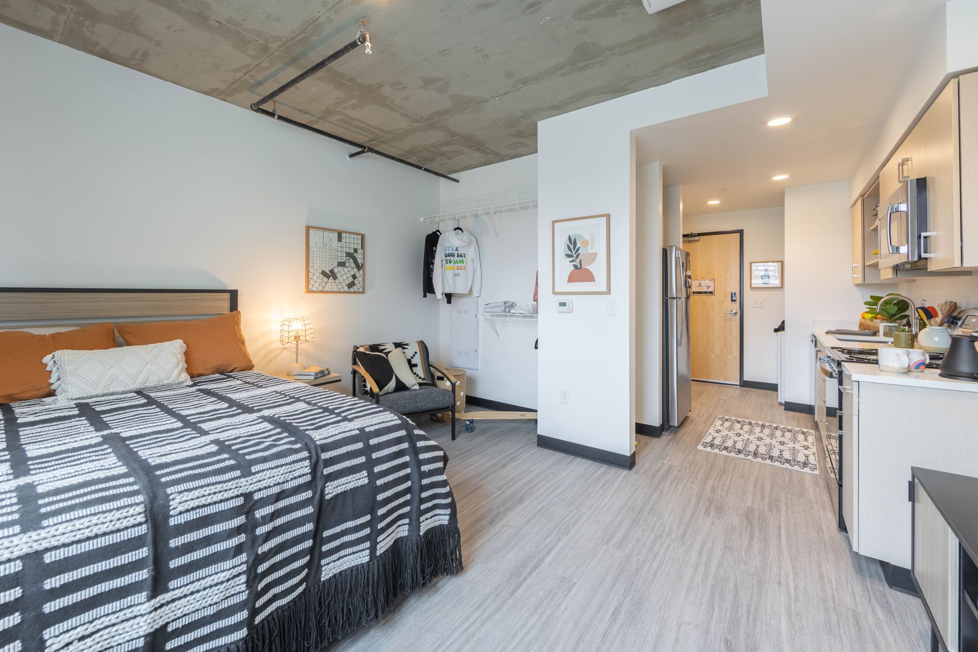 Modern studio bedroom with bed, kitchenette, and hallway in a bright apartment