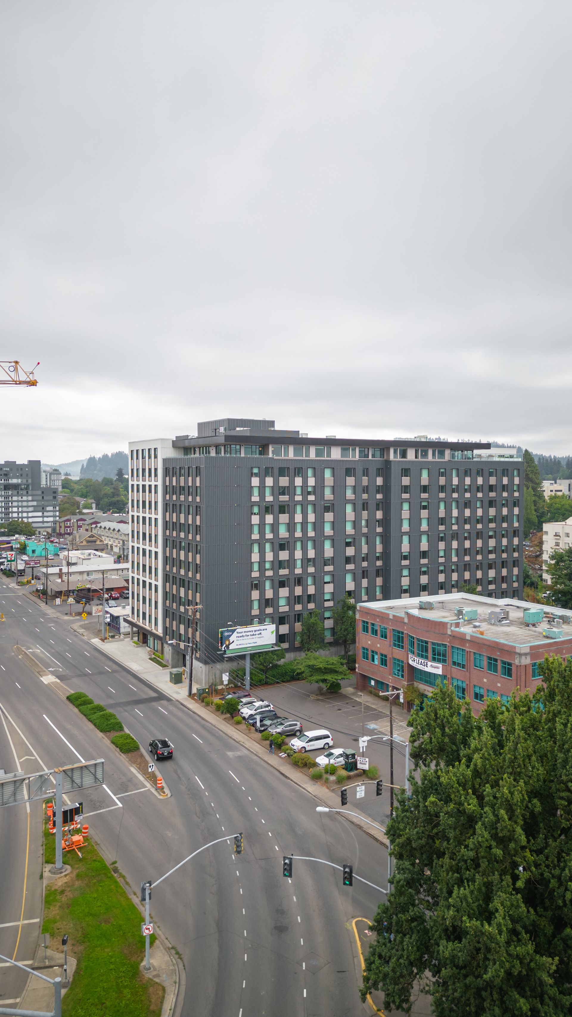 City street with a tall gray apartment building and light traffic on an overcast day