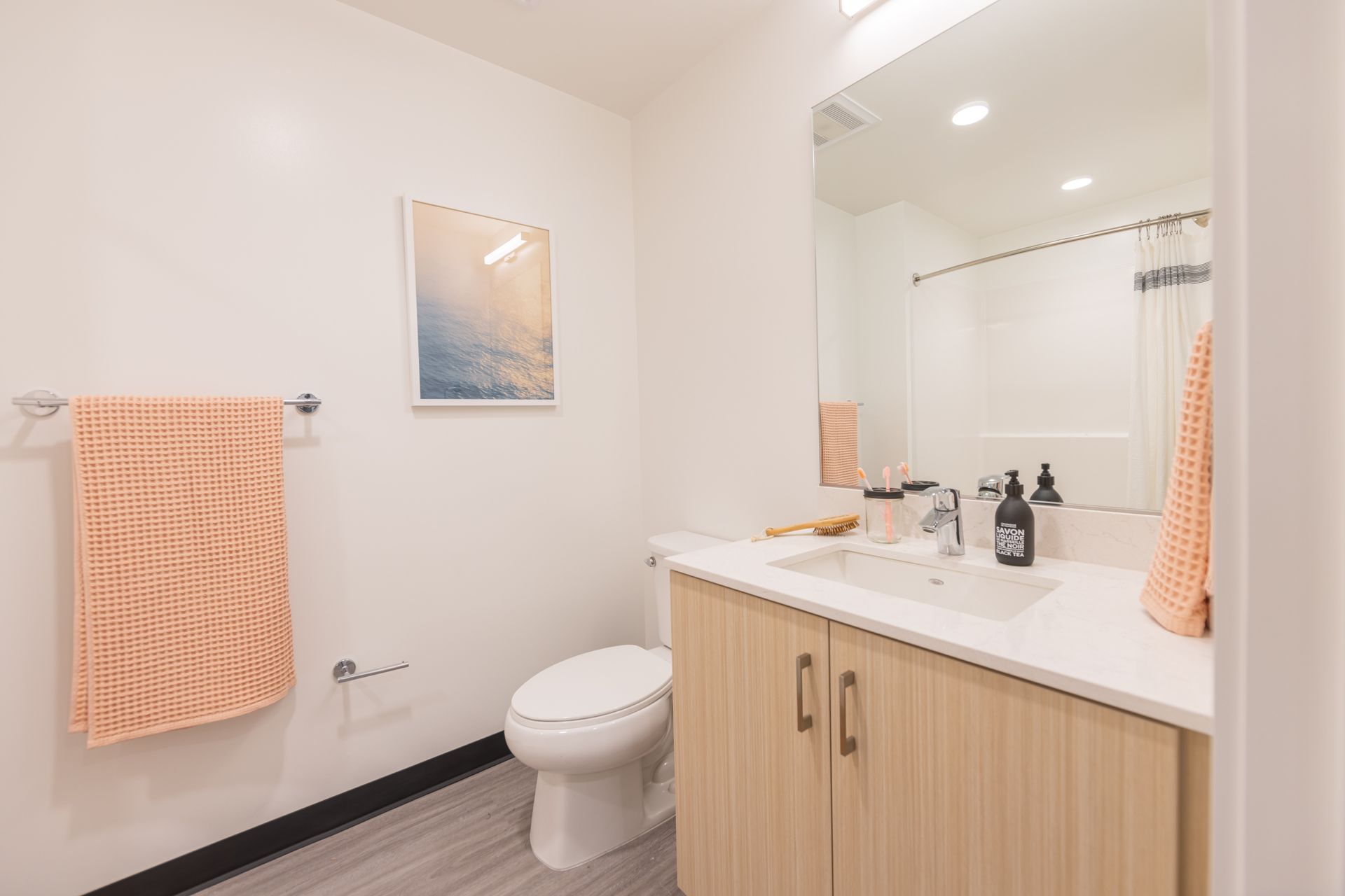 Small bright bathroom with toilet, vanity sink, mirror, and peach towels
