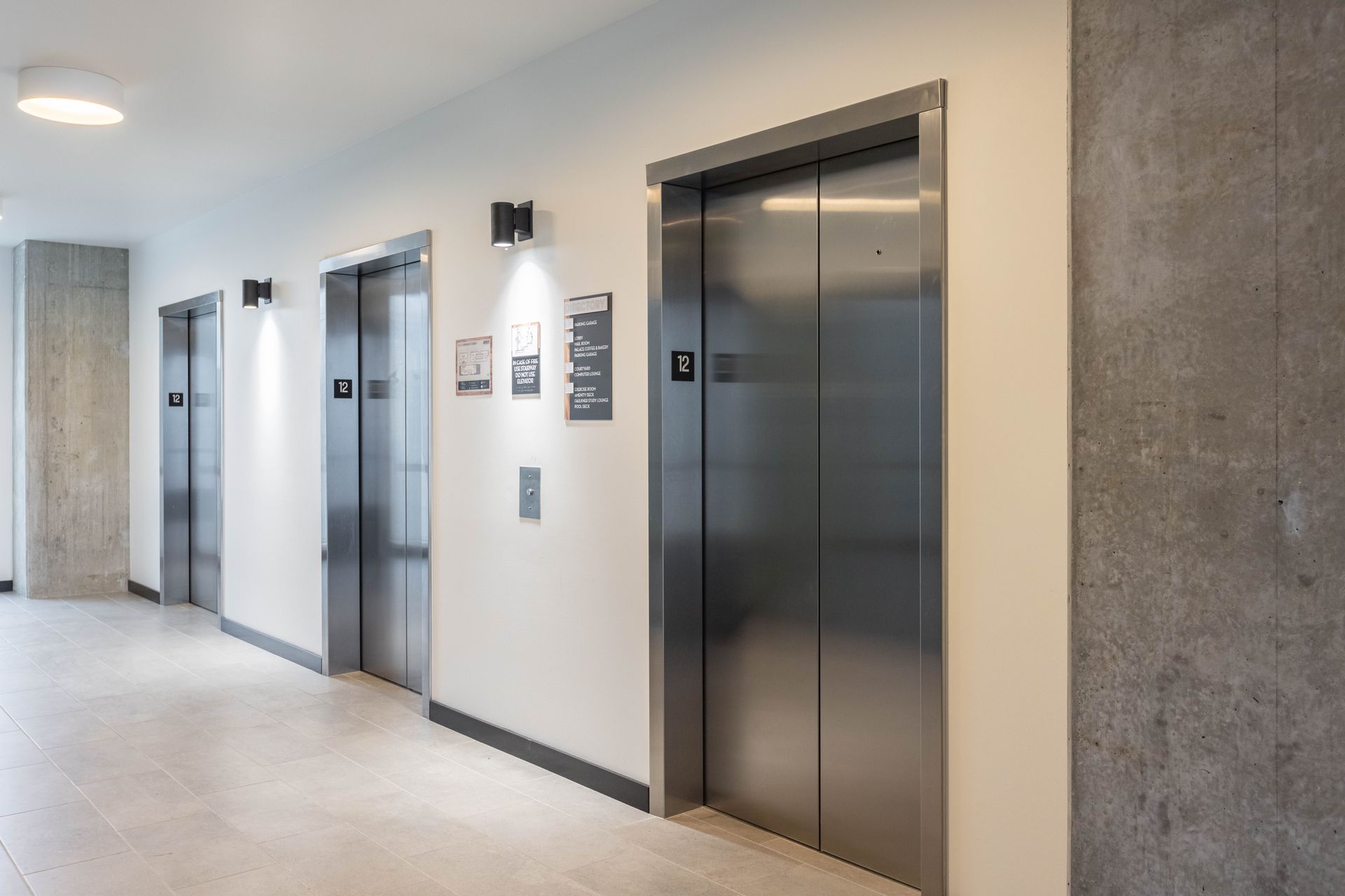 Hallway with three stainless steel elevator doors and wall lights in a modern building