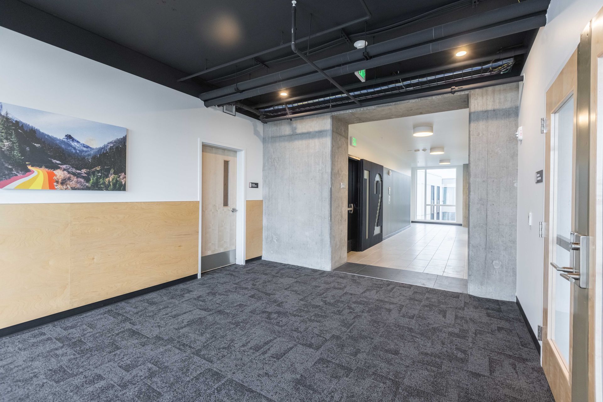 Empty modern office lobby with carpeted floor, concrete walls, and bright hallway beyond