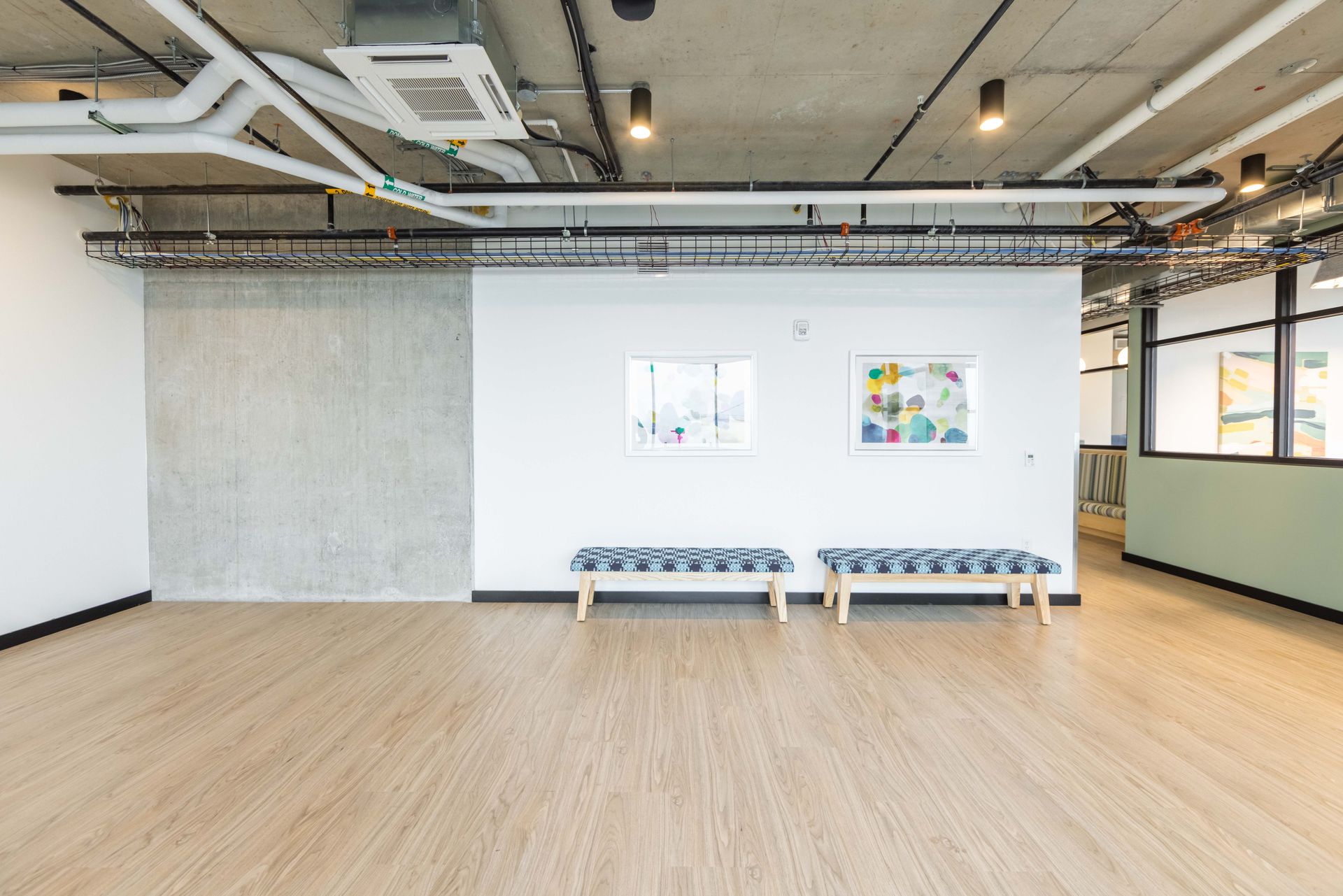 Spacious modern studio with wood floor, exposed ceiling, and benches against a white wall