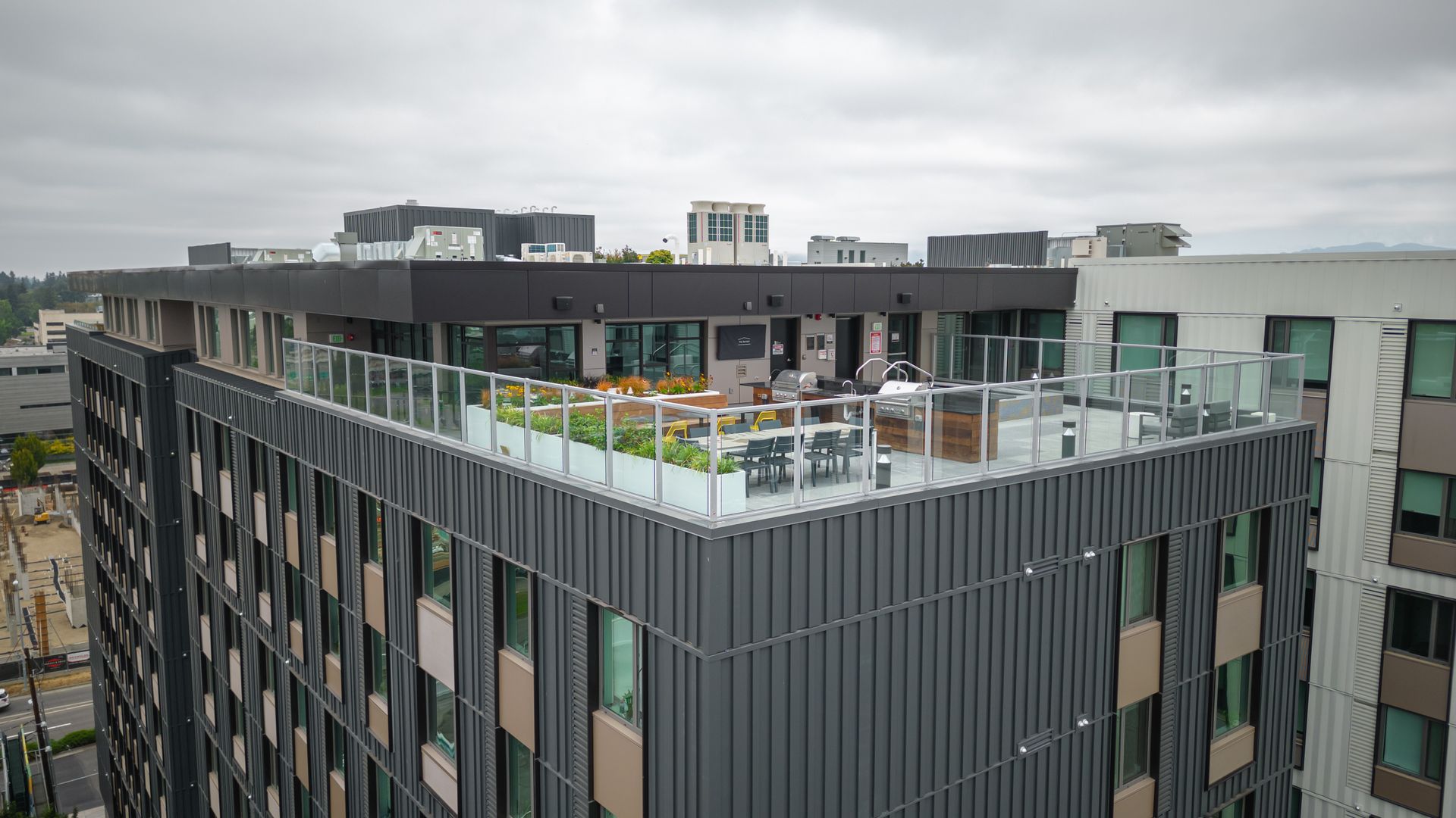 Rooftop terrace atop a modern apartment building, with greenery and seating on a cloudy day