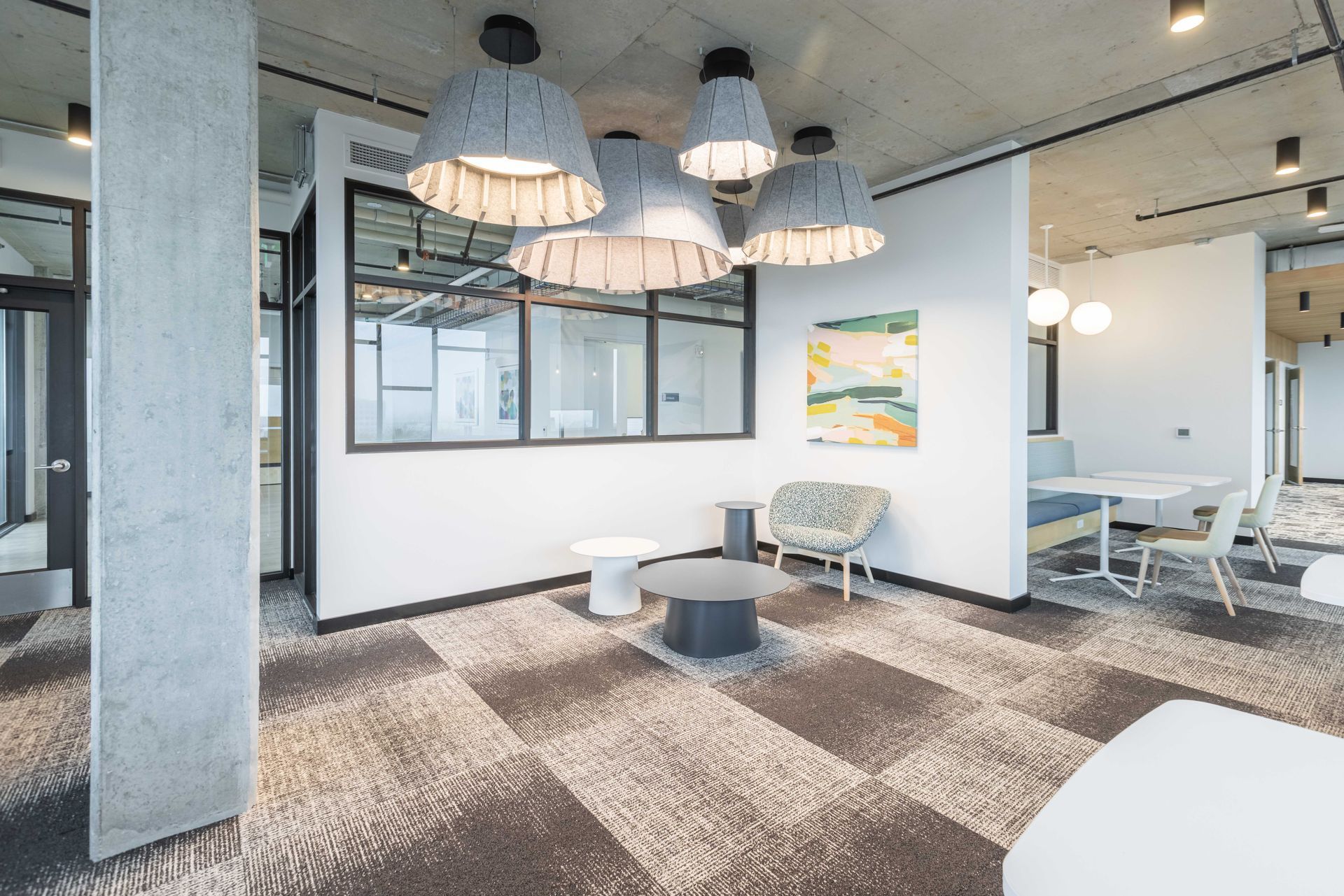 Modern office lounge with hanging pendant lights, carpeted floor, and white chairs and tables