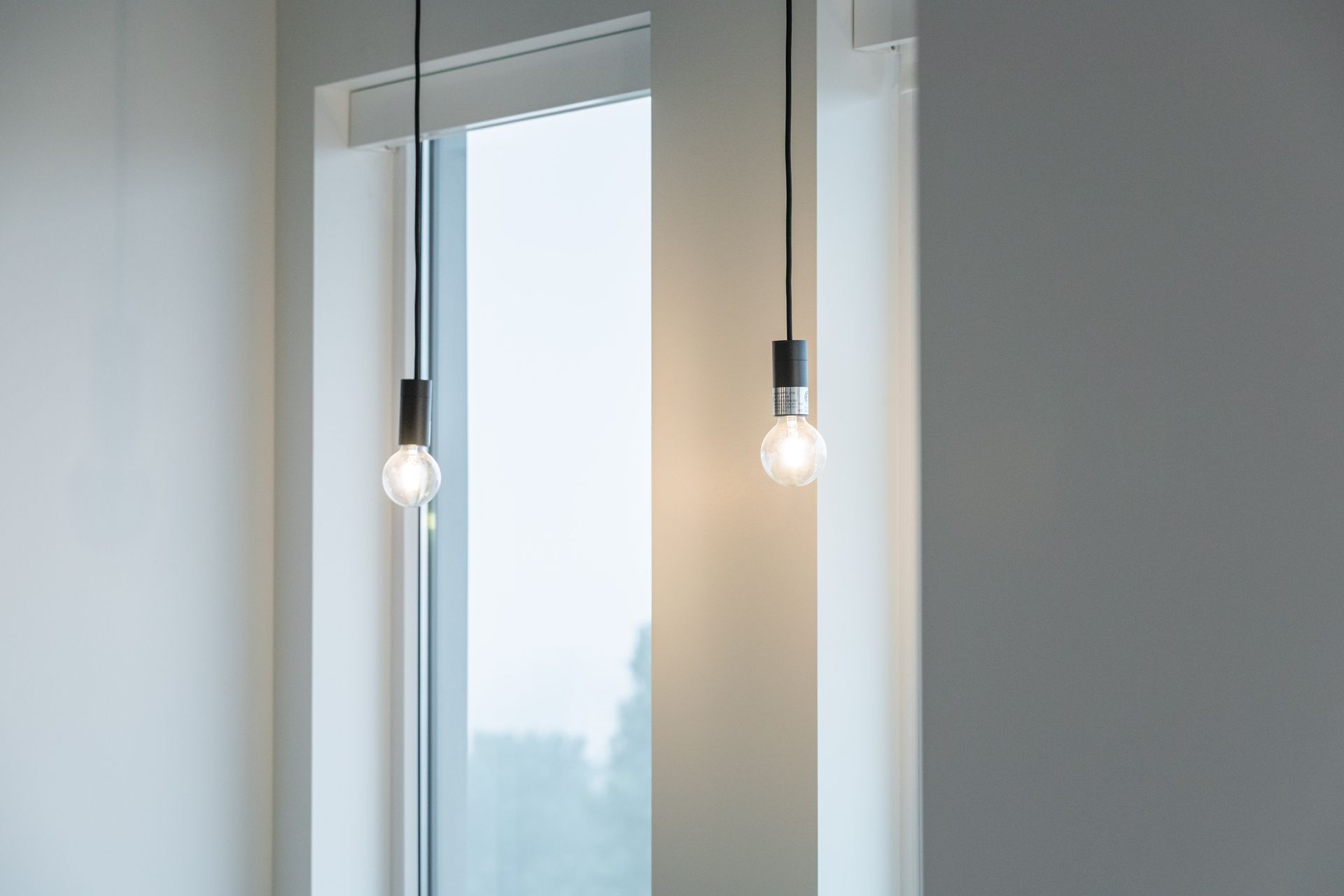 Two pendant bulbs hanging beside a tall window in a bright minimalist room