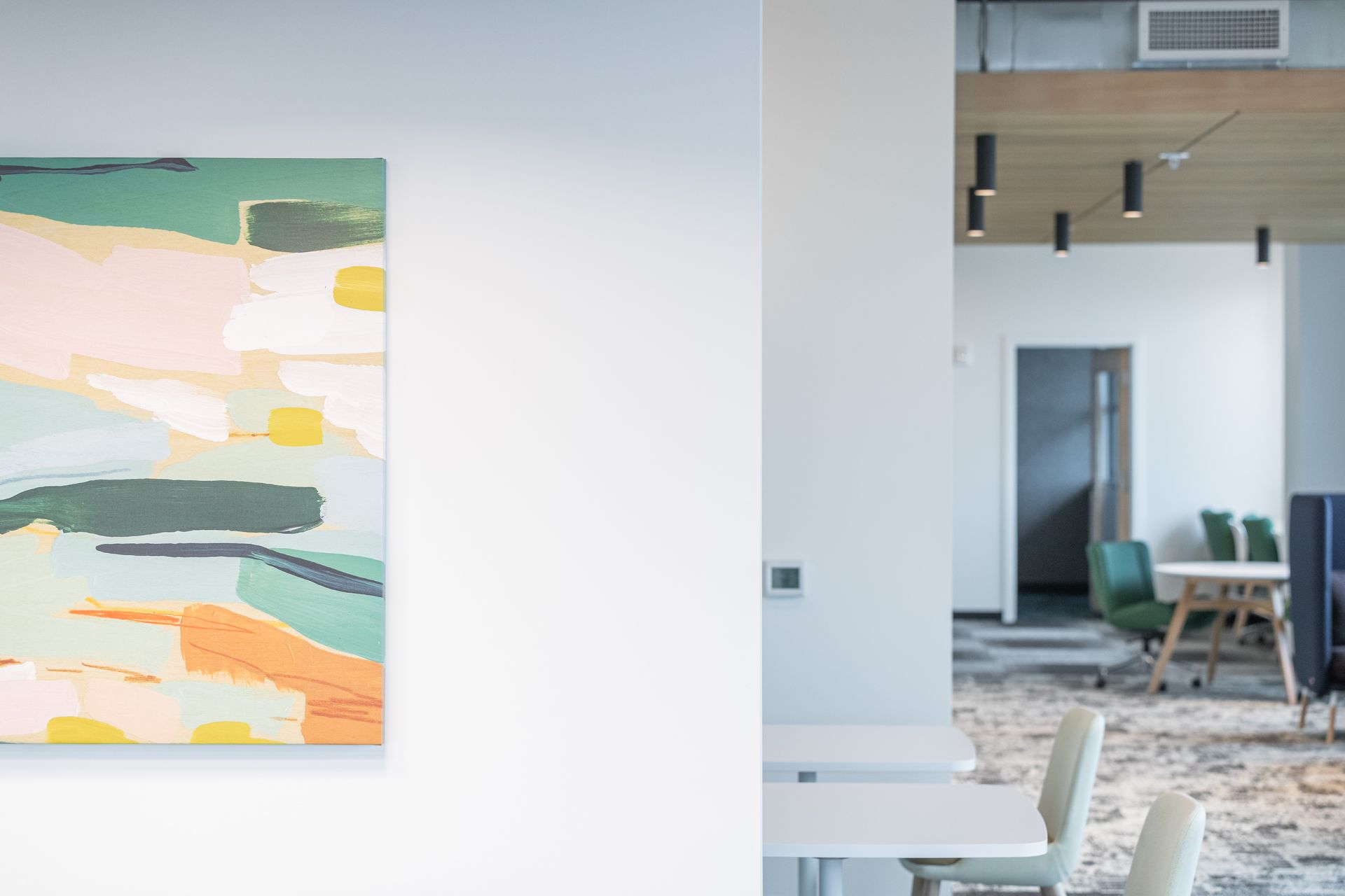 Abstract colorful painting on a white gallery wall beside a modern seating area and doorway