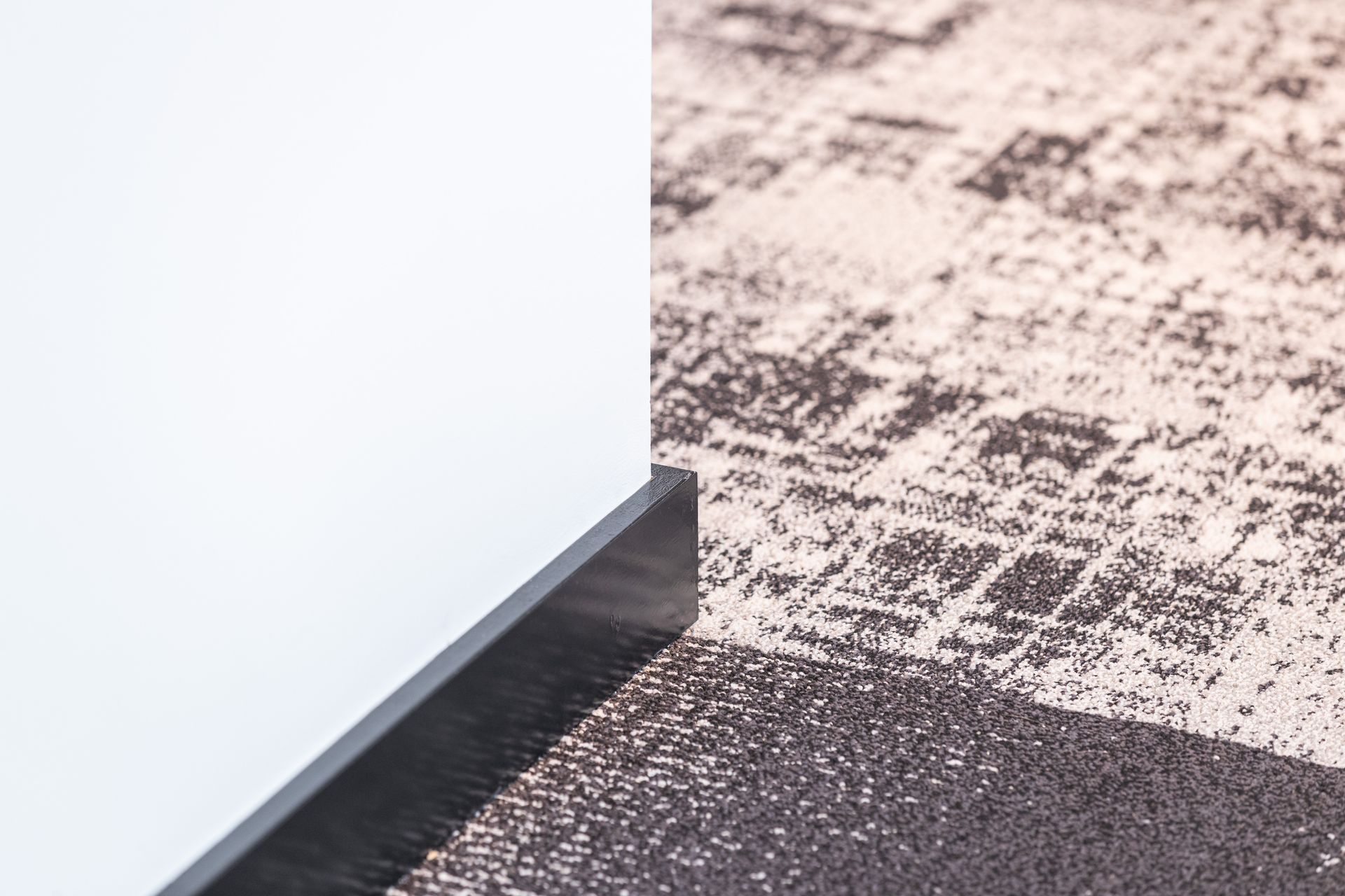 White wall corner with gray baseboard beside a textured black-and-white carpet edge