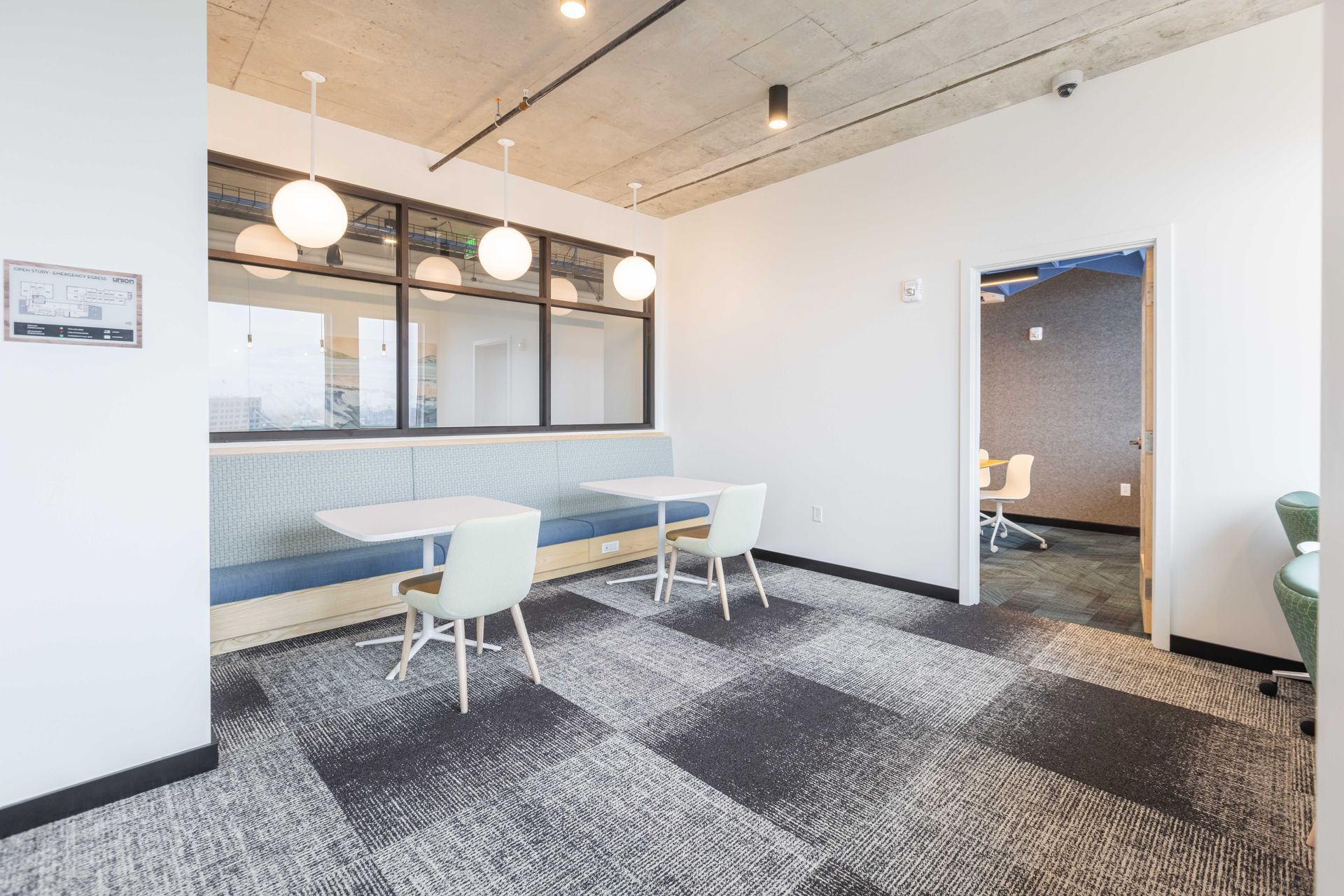 Bright modern office lounge with white chairs, long table, and large windows through black-framed glass wall