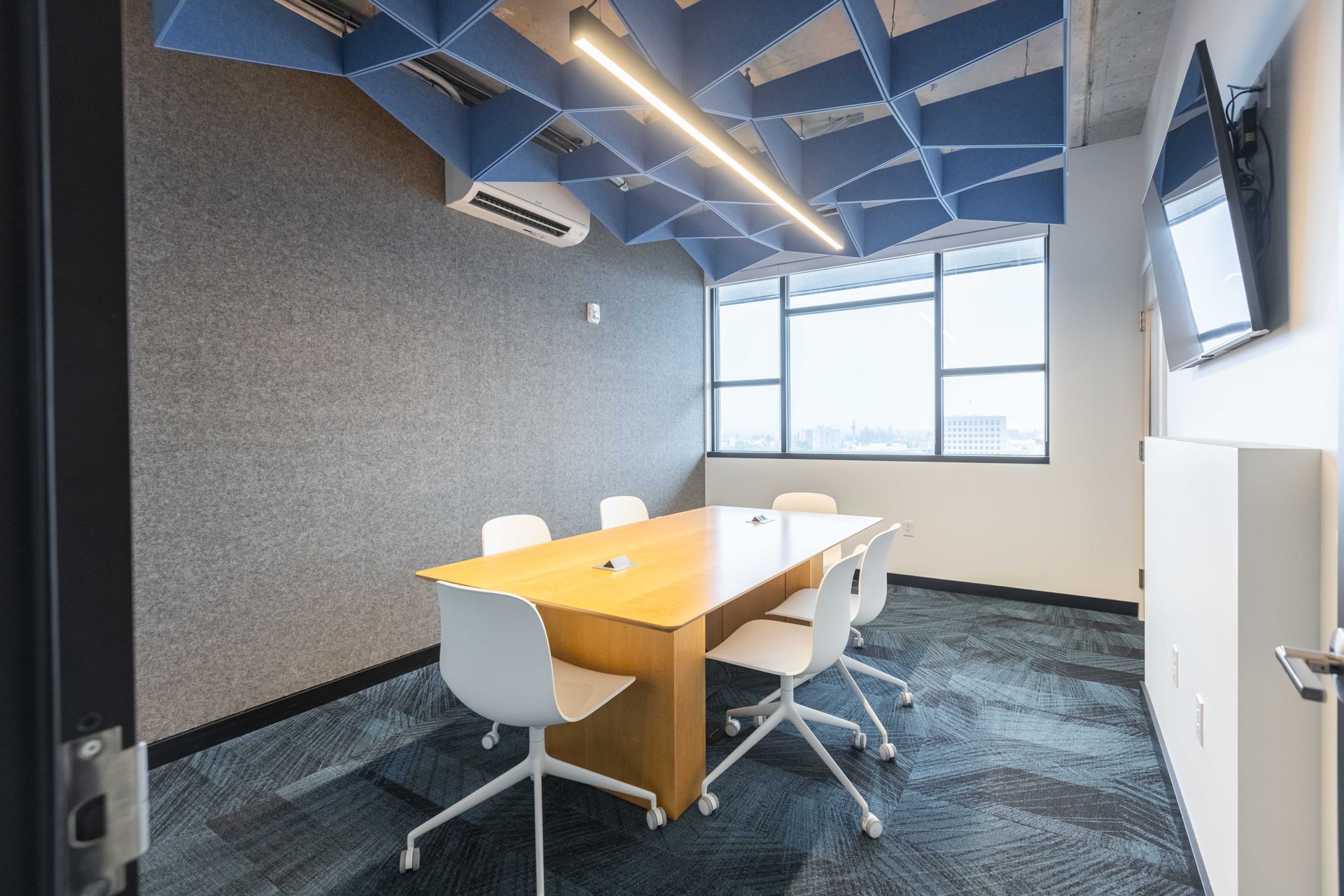 Modern office meeting room with a wooden table, white chairs, and large windows under a blue ceiling